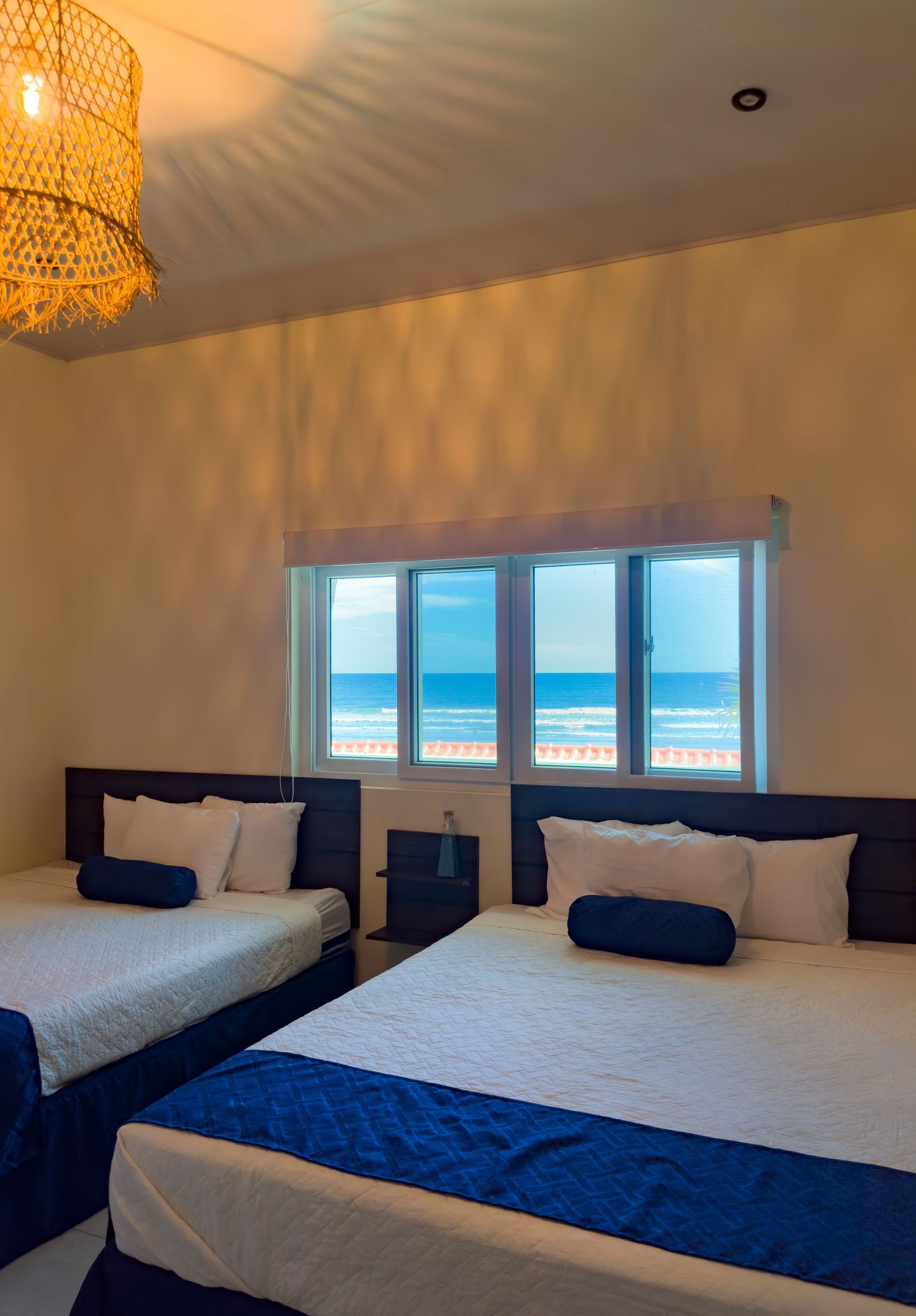 Habitación con dos camas queen y vista al mar. Las camas tienen detalles en azul.