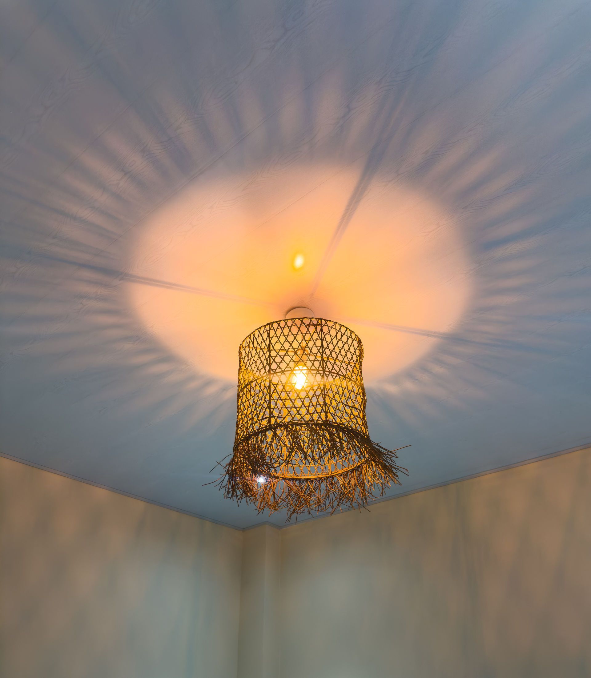 Lámpara decorativa estampada que cuelga del techo y proyecta luz y sombras en un rincón de la habitación.