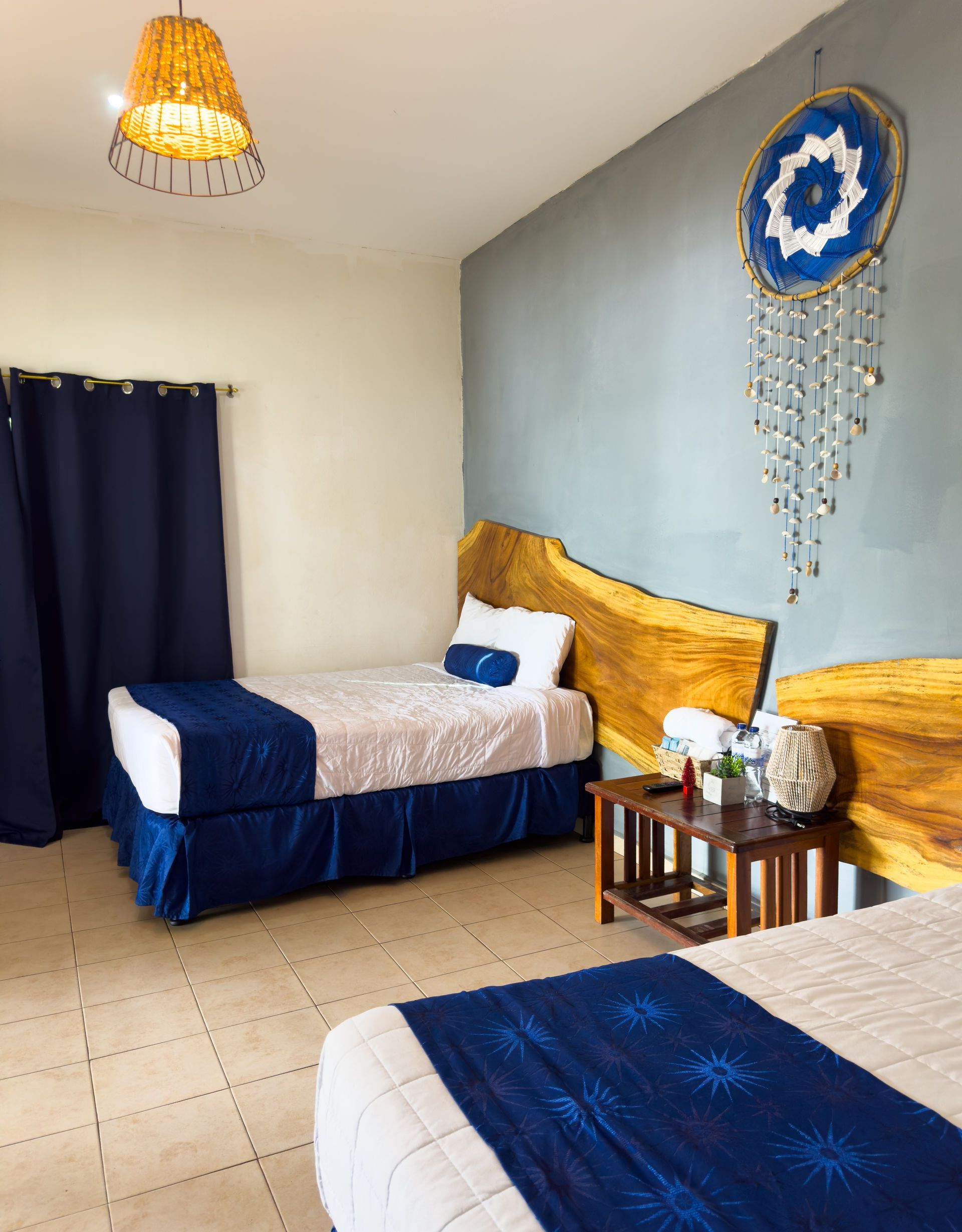 Dos camas individuales con detalles azules en una habitación con un atrapasueños en una pared azul.