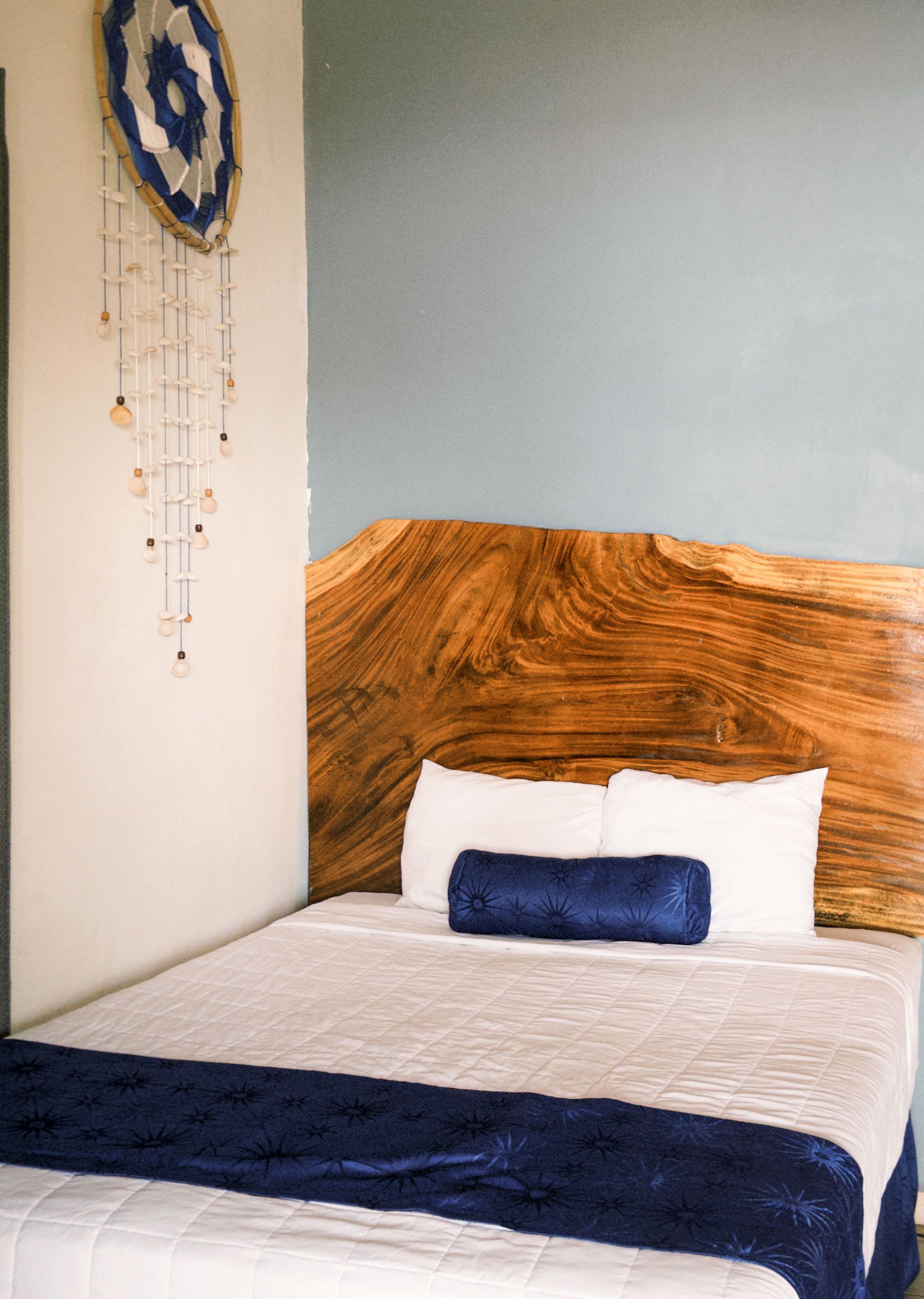 Dormitorio con cabecero de madera, ropa de cama blanca, detalles en azul y un tapiz colgante.