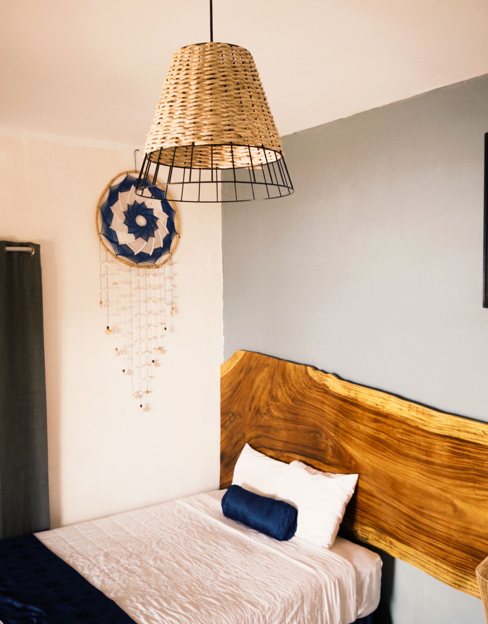 Dormitorio con cama individual con cabecero de madera, decorado con atrapasueños y lámpara tejida.