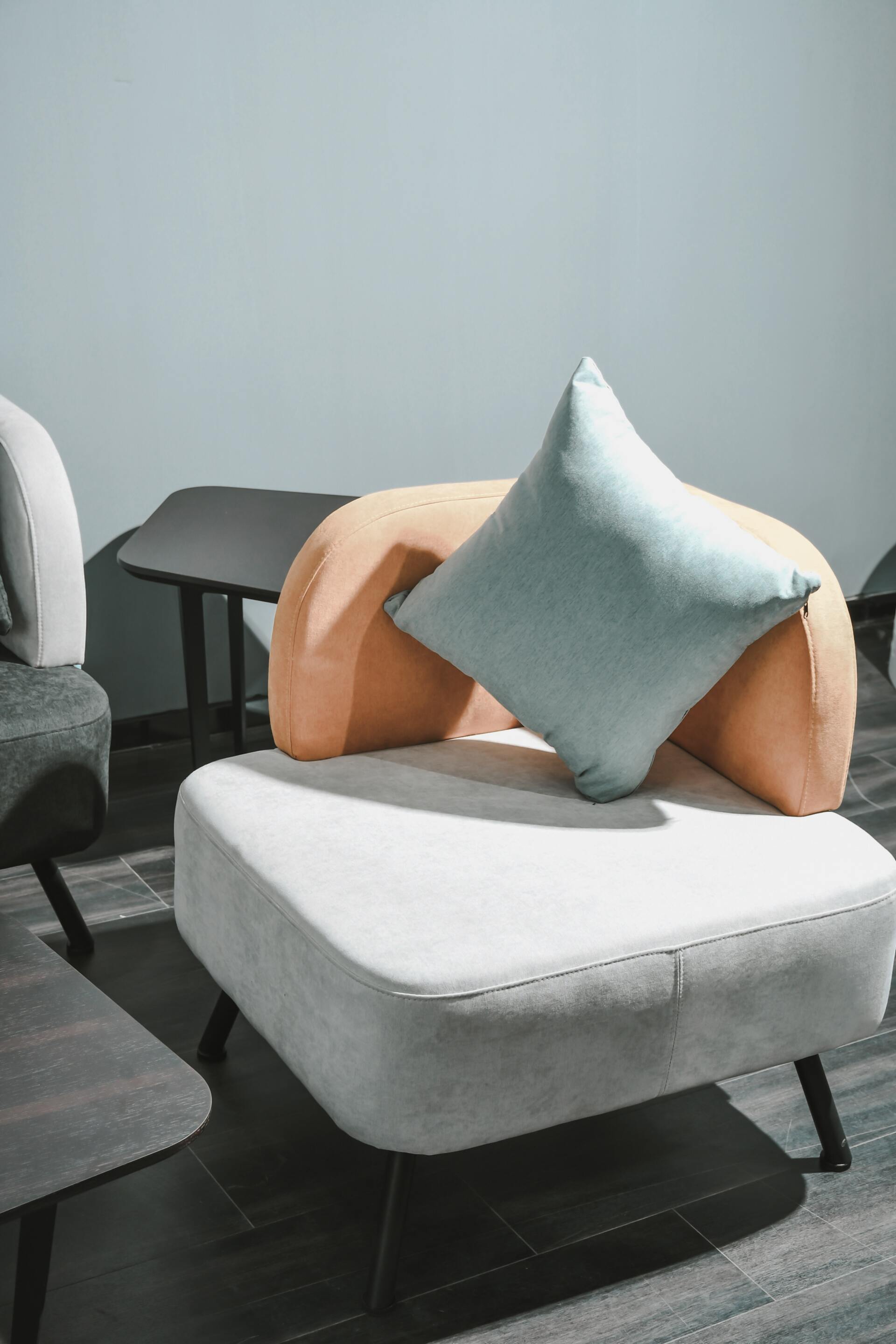 Sillón moderno con almohada azul claro, apoyado sobre una pared gris.