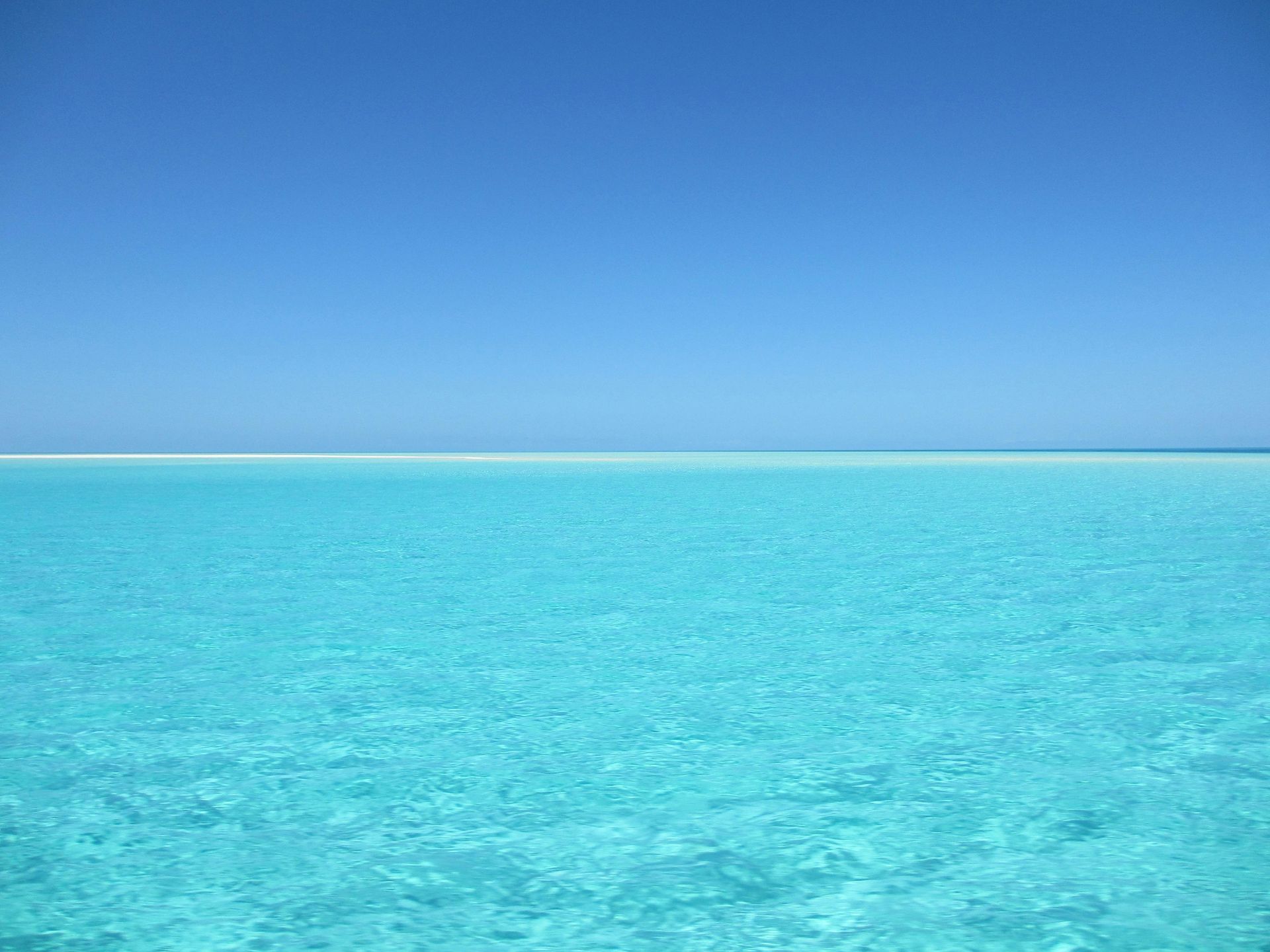 Océano turquesa vibrante bajo un cielo azul claro y brillante, línea del horizonte visible.