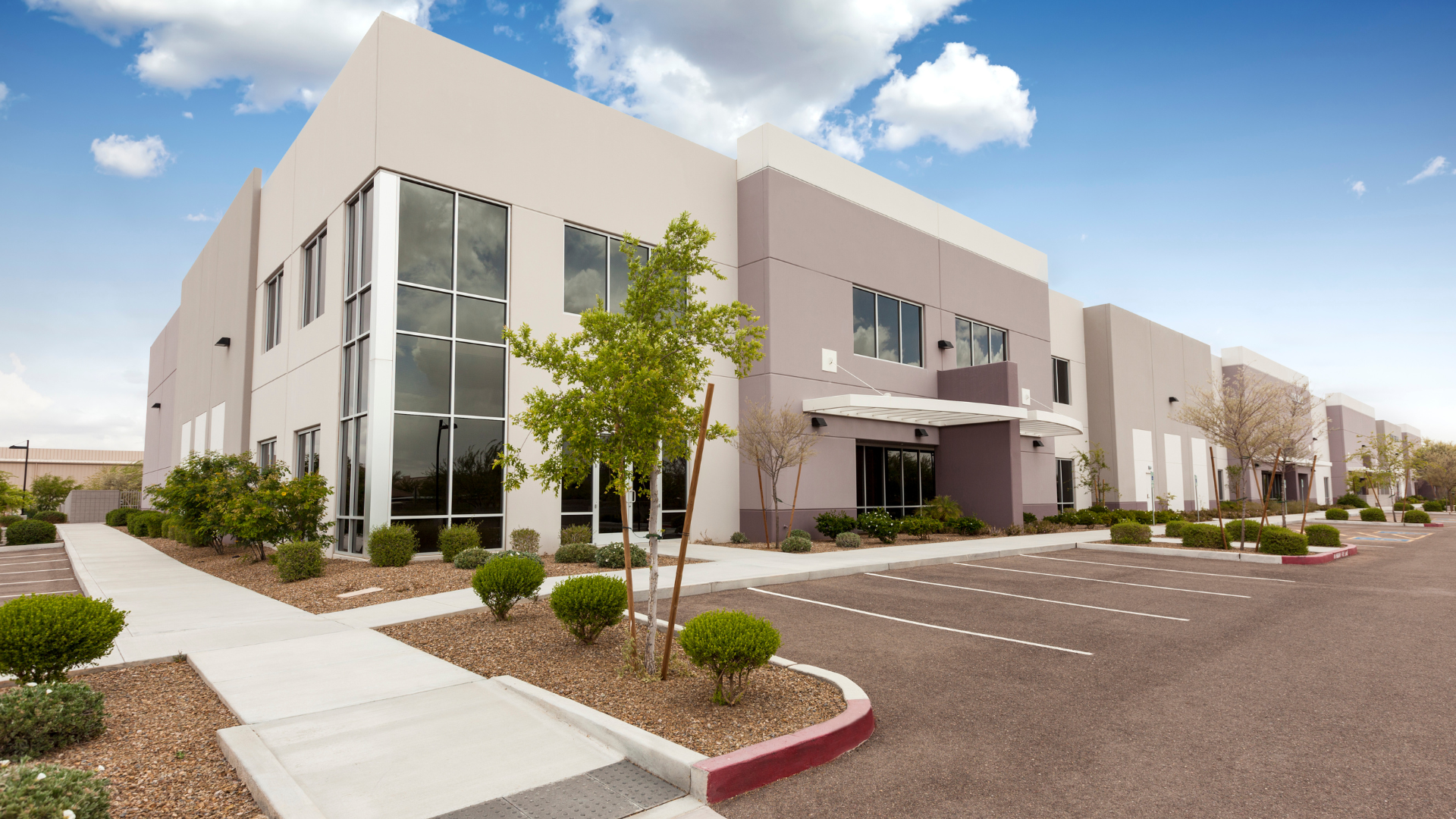Modern commercial building with tan and purple exterior; blue sky; parking lot.