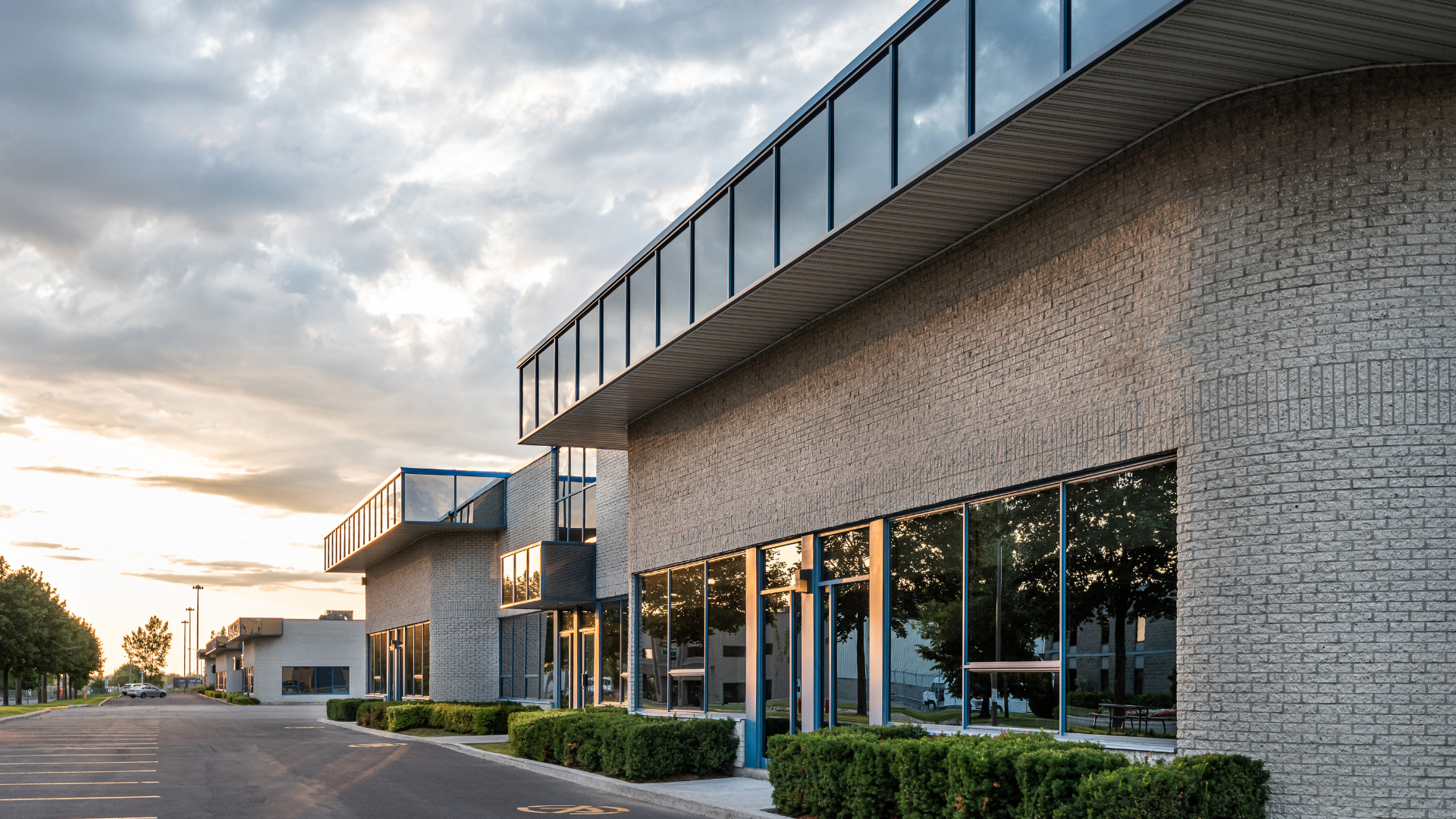 Modern brick building with glass windows, reflecting trees and sky, in an overcast setting.