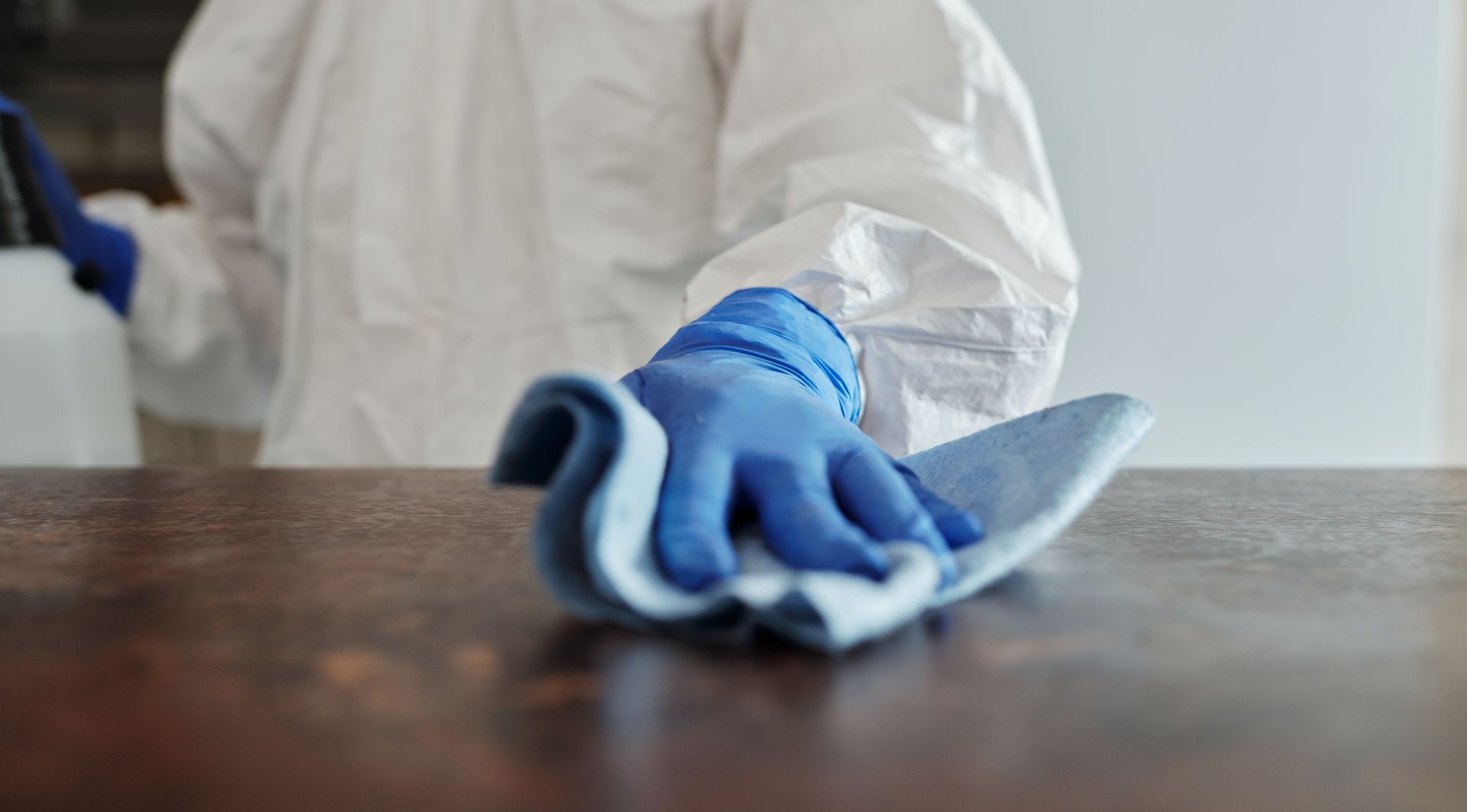 A person wearing blue gloves is cleaning a wooden table with a cloth.