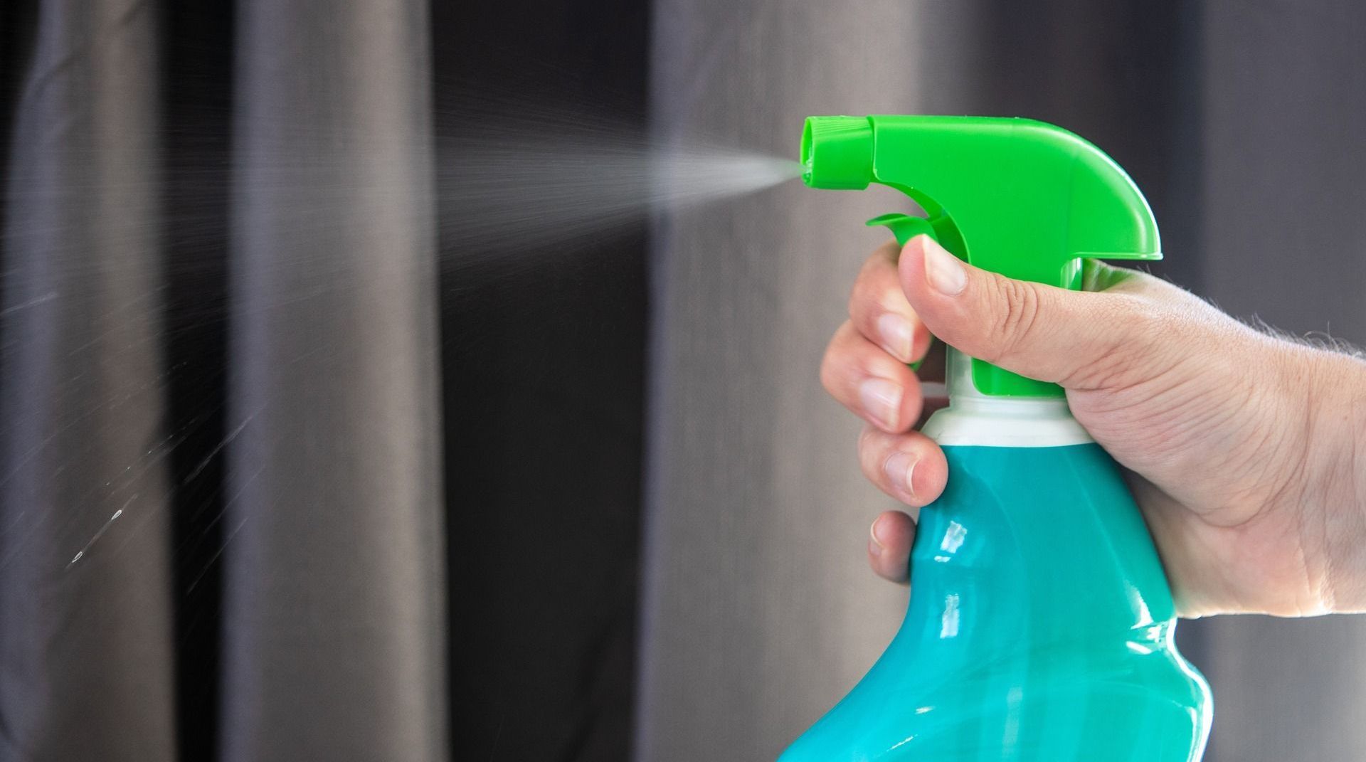 A person is holding a spray bottle in their hand and spraying it on a curtain.