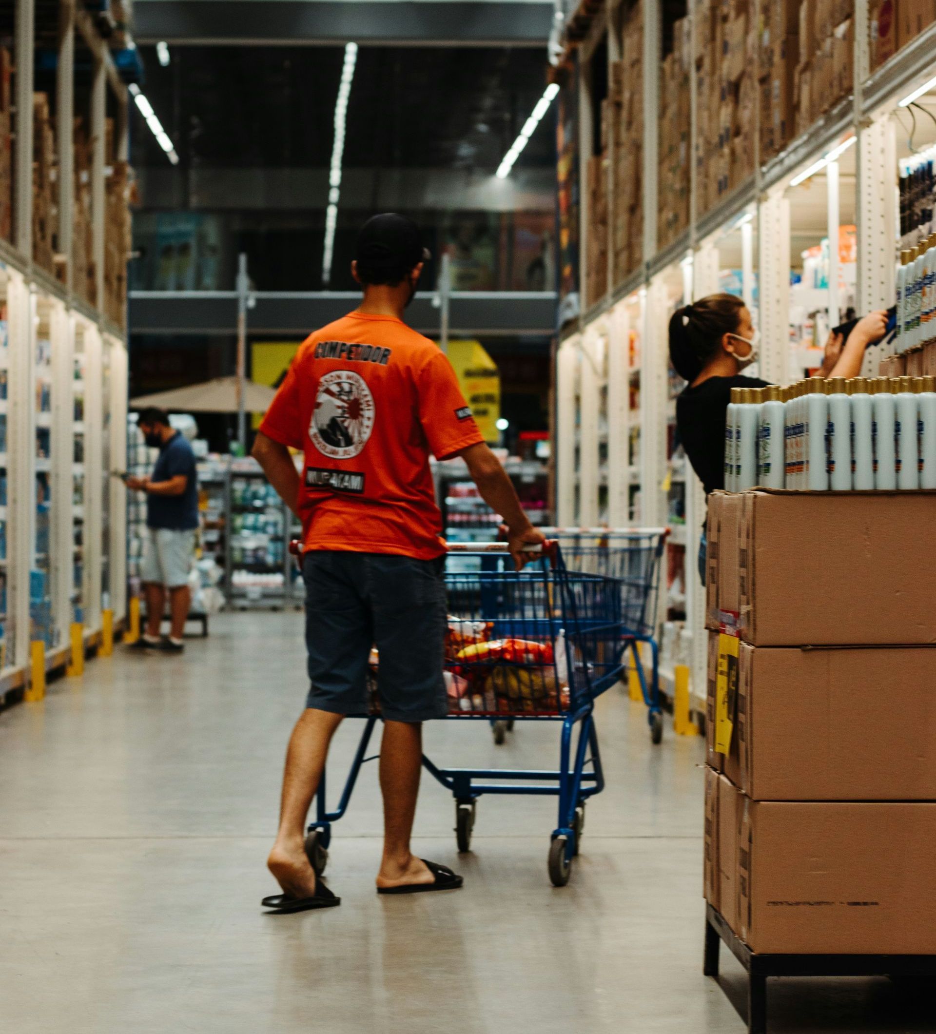 A man in an orange shirt is pushing a shopping cart