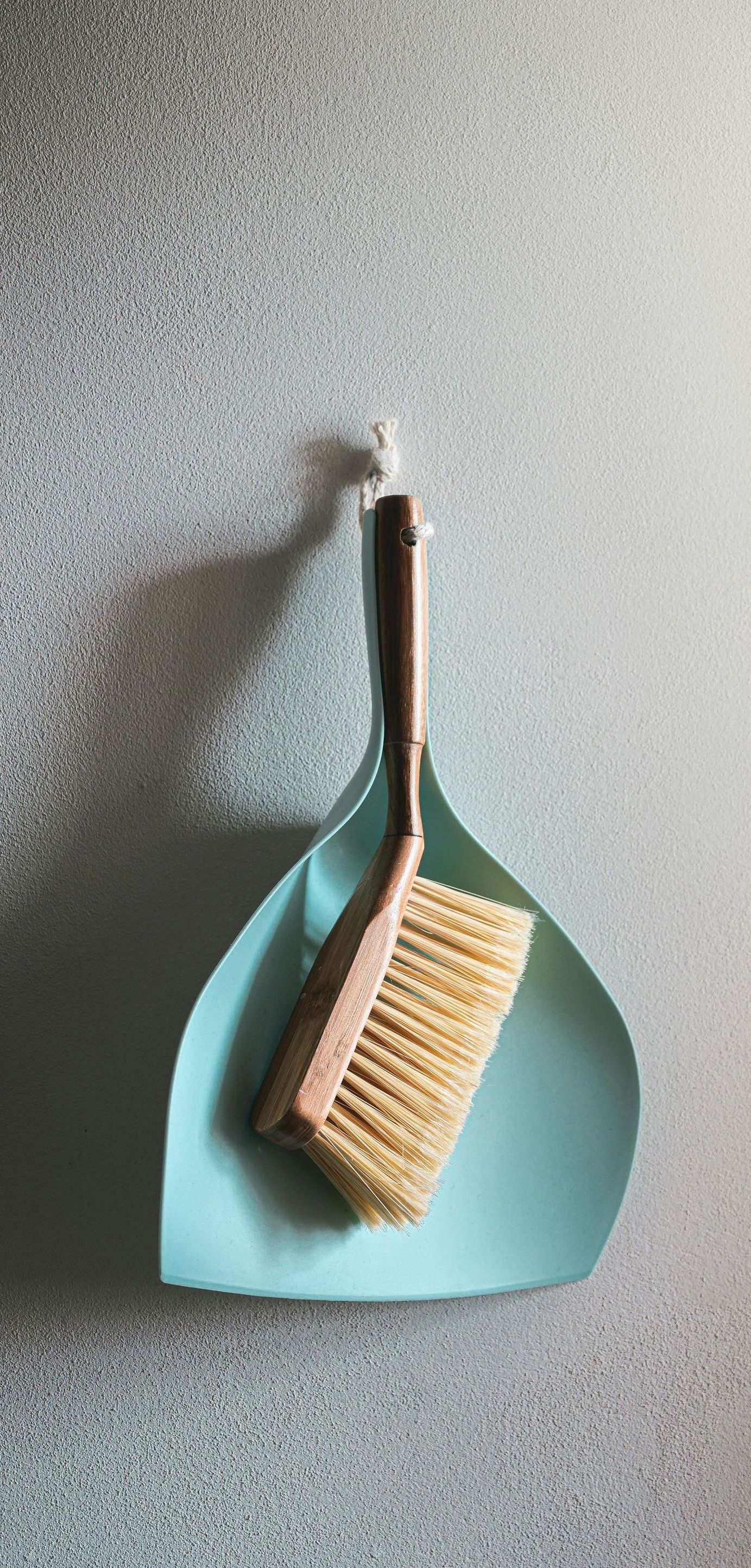 A brush and dustpan are hanging on a hook on a wall.
