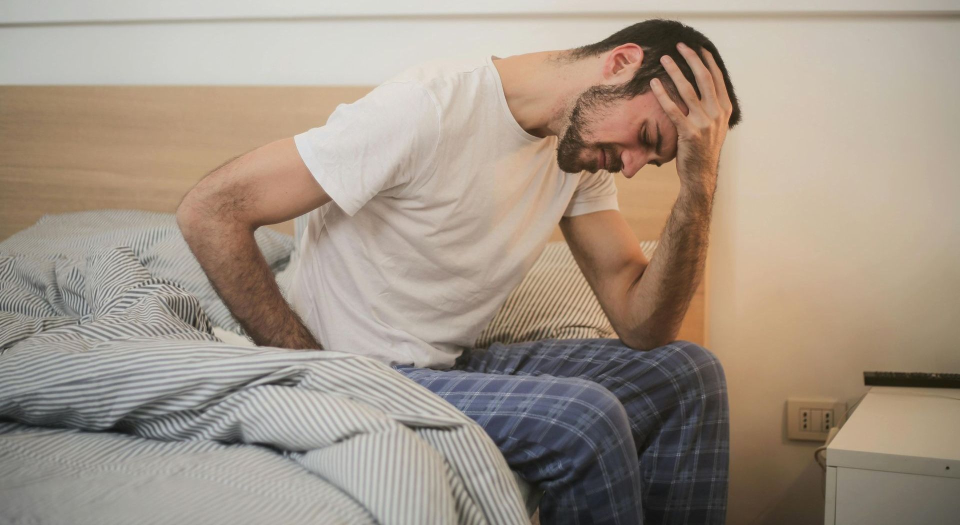 A man is sitting on a bed with his head in his hands.