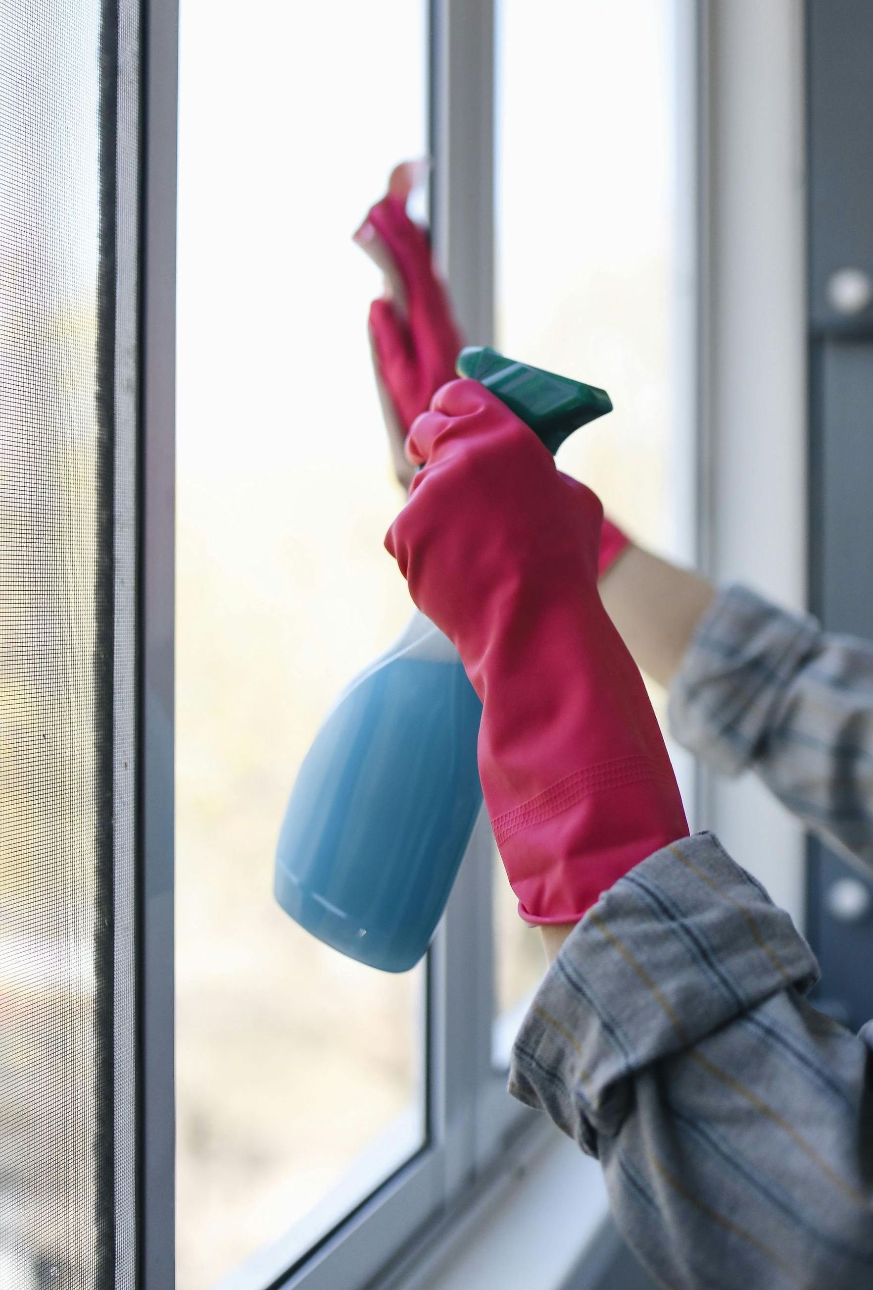A person wearing red gloves is cleaning a window with a spray bottle.
