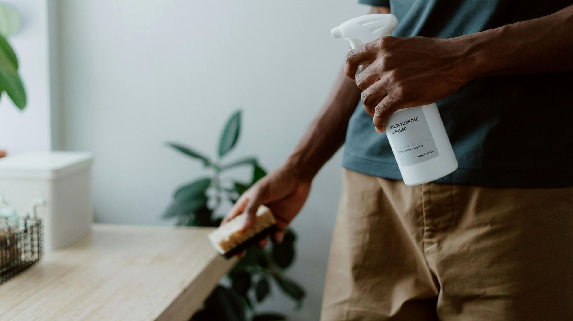A man is cleaning a table with a spray bottle and a sponge.