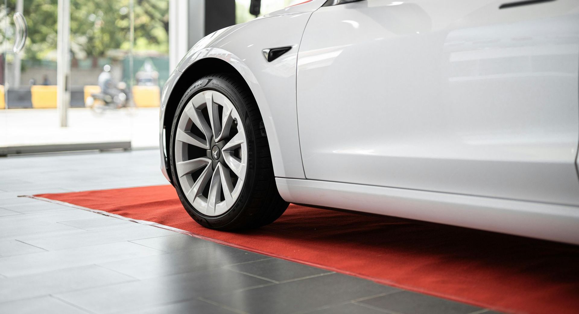 A white tesla model 3 is parked on a red rug in a showroom.