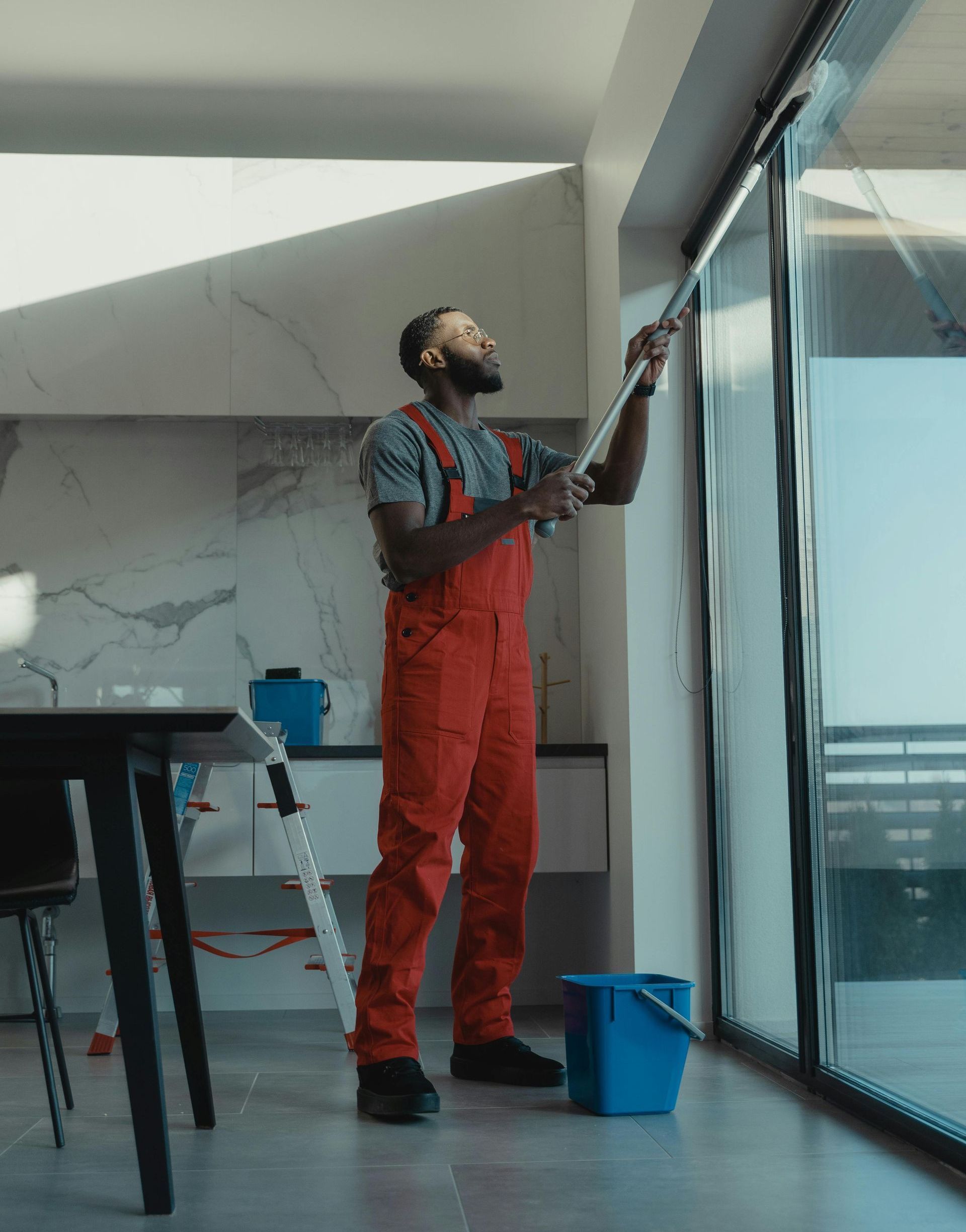 A man in red overalls is cleaning a window with a mop.