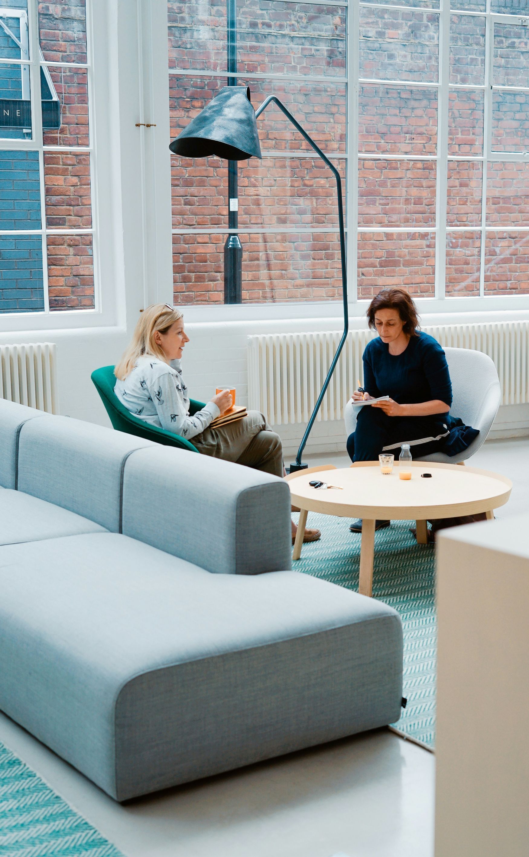 Two women are sitting on a couch talking to each other in a living room.