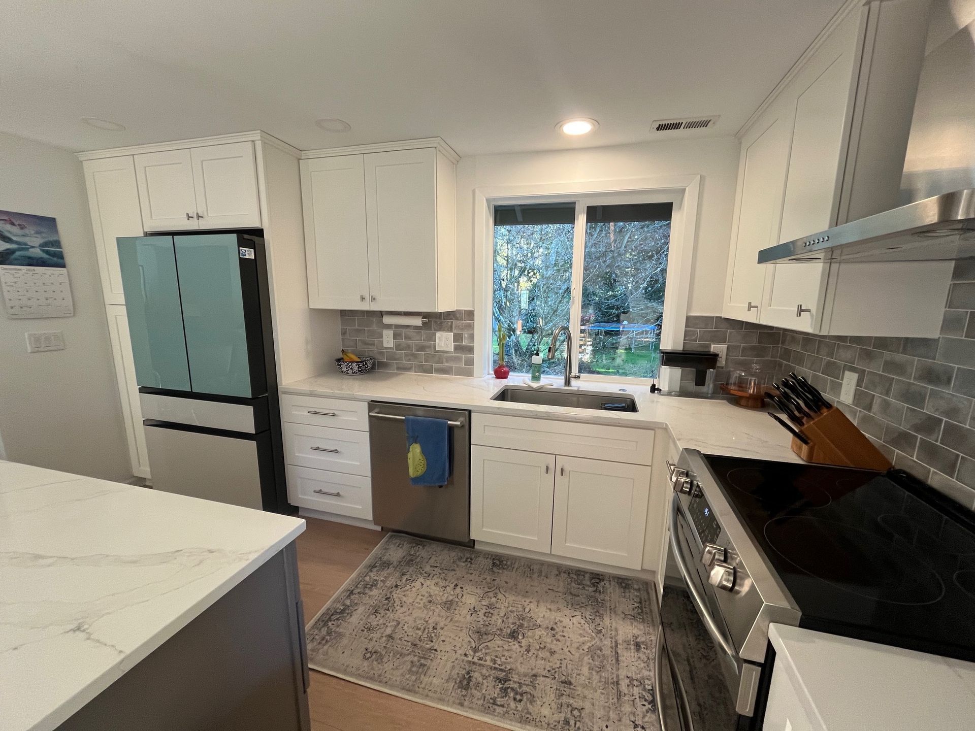 A different view of a beautiful modern kitchen featuring sleek white cabinets, state of the art fridge, granite top island, new floors.