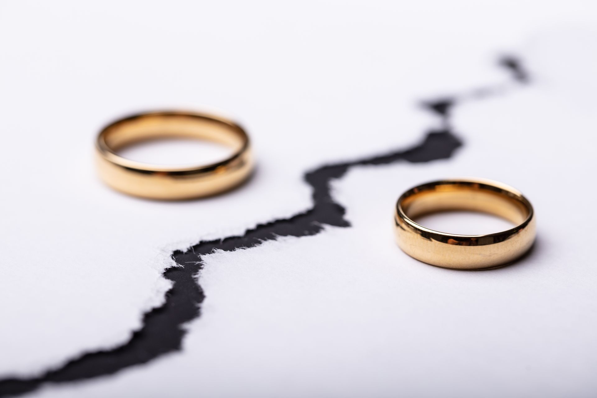 Two gold wedding rings sit on either side of a torn white paper, suggesting legal separation