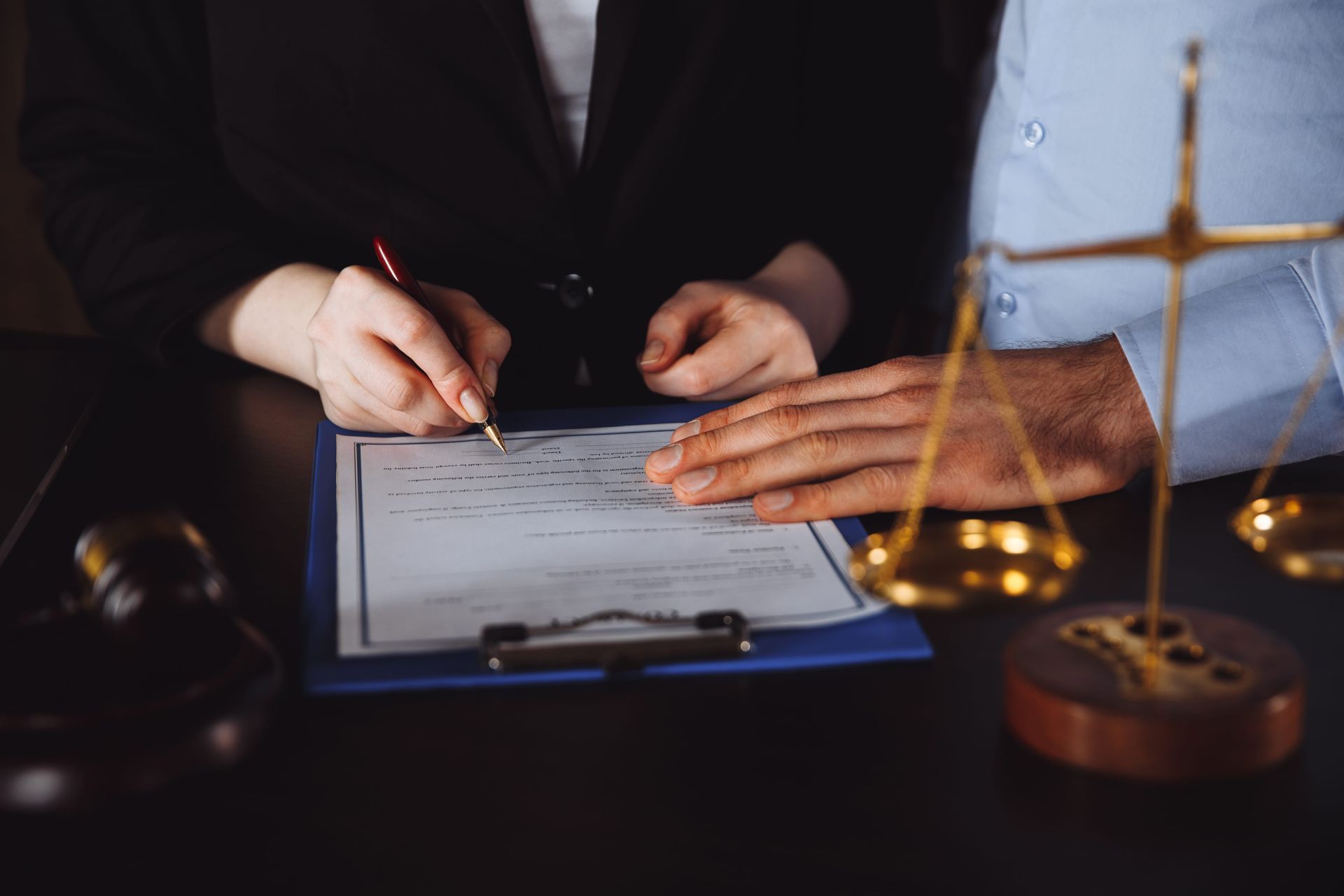 Hands signing a document on a clipboard beside a gavel and scales of justice