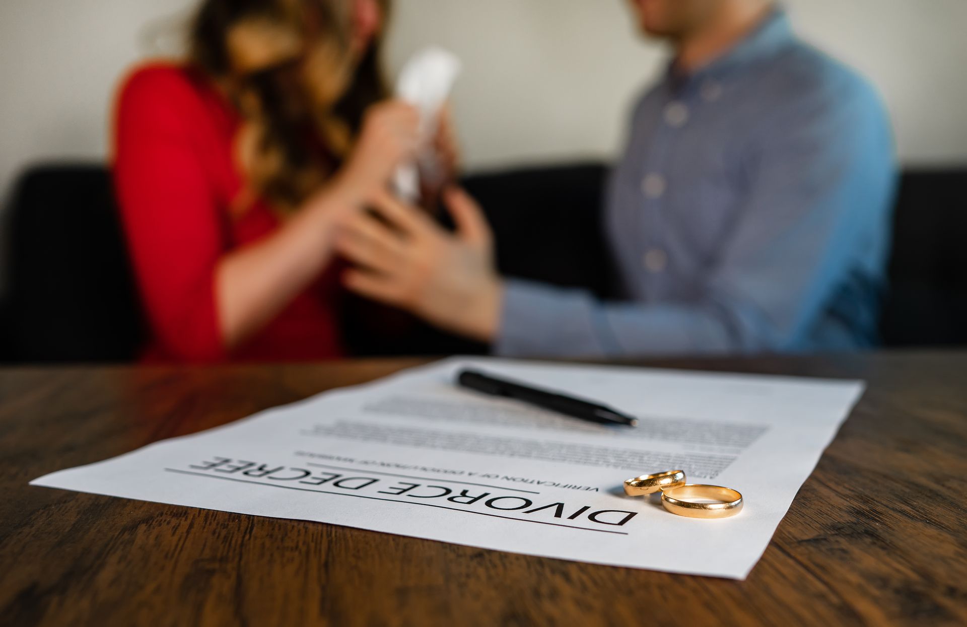 Divorce decree with rings and a couple arguing in the background.