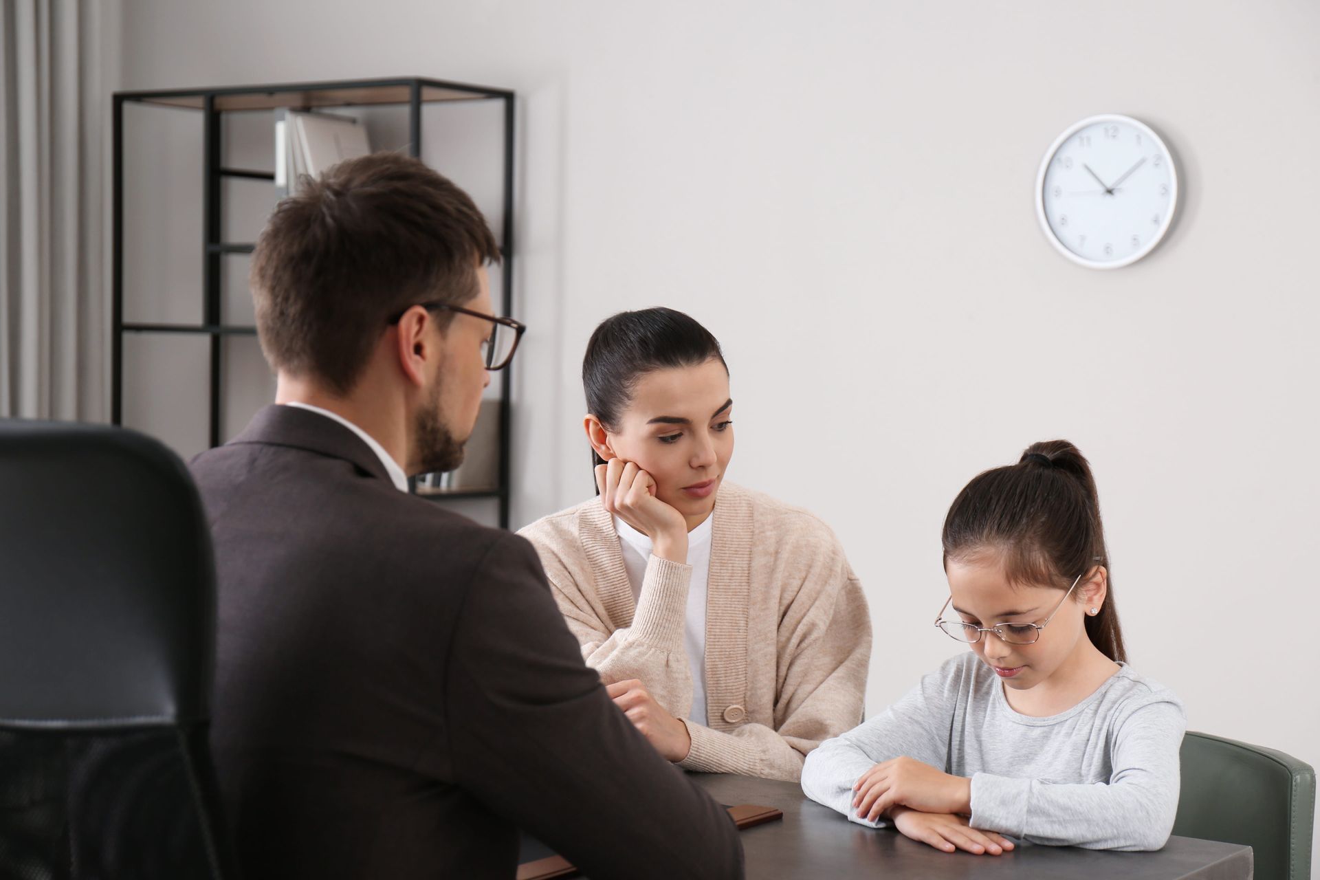 Three people in a meeting room reviewing papers at a table, with a wall clock behind them.
