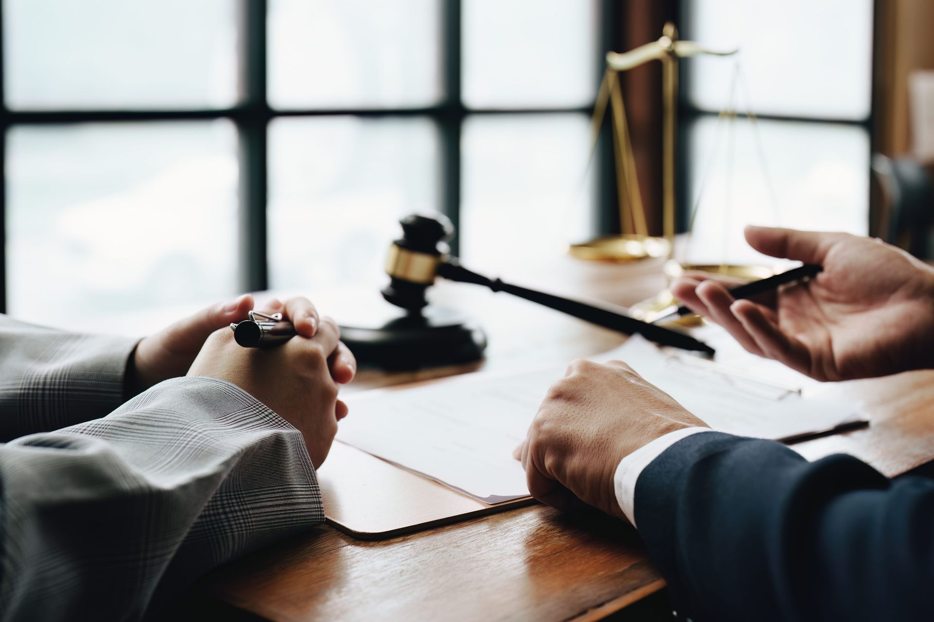 People in suits discussing documents at a desk with a gavel and scales of justice.