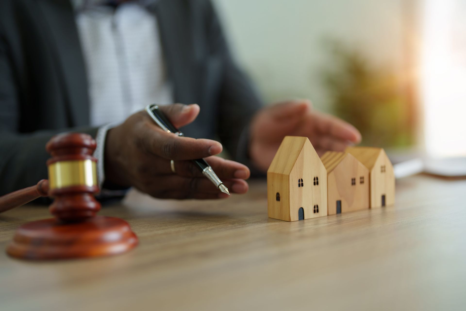 Hand holding pen beside small house models and gavel on a desk, suggesting property or legal matters