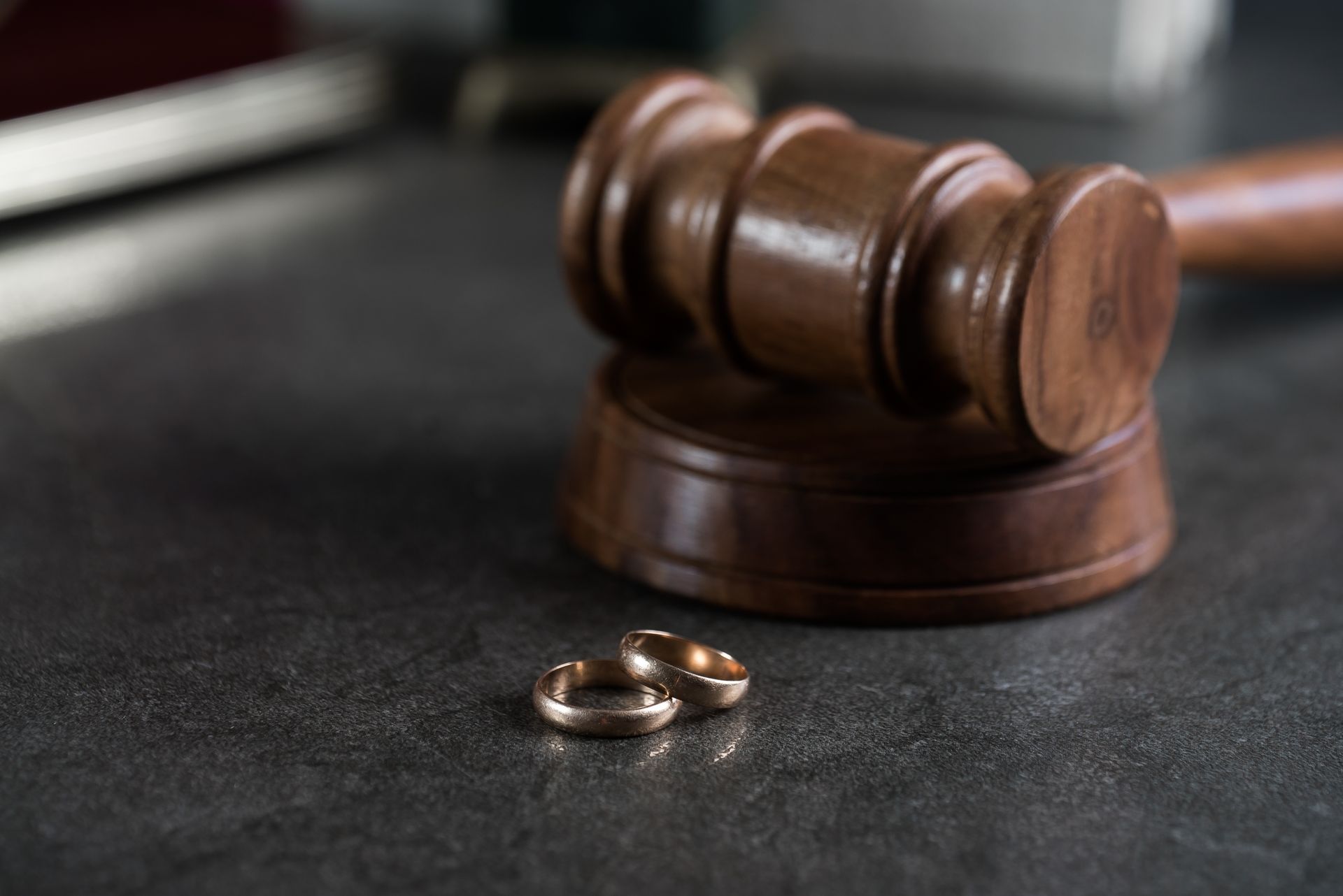 Gavel and two wedding rings on a dark surface, symbolizing divorce.