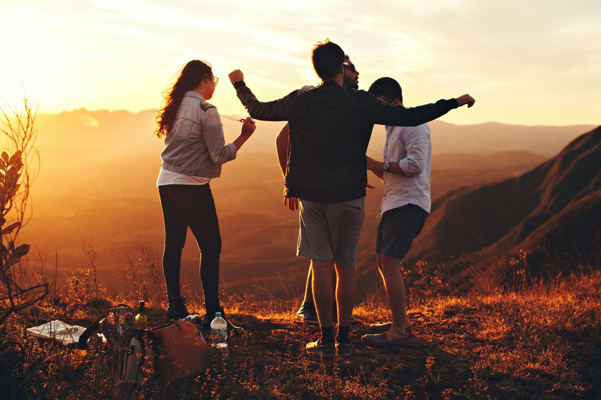 People watching the sunset from a mountaintop. Warm light illuminates the group; one raises arms.
