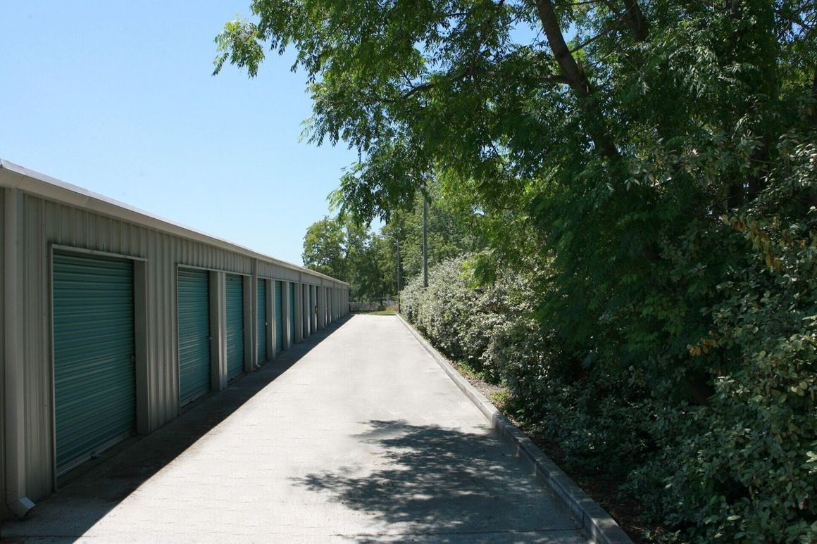 Row of teal storage unit doors with a paved path and trees on the right.