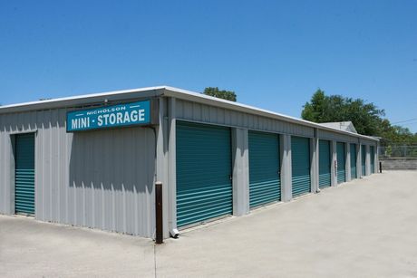 Sign for Nicholson Mini Storage and Salon, blue and white, with storage units in background.