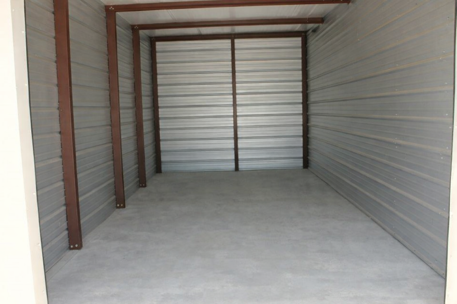 Empty storage unit with a lawnmower and flamingo decoration. Steel walls and frame.
