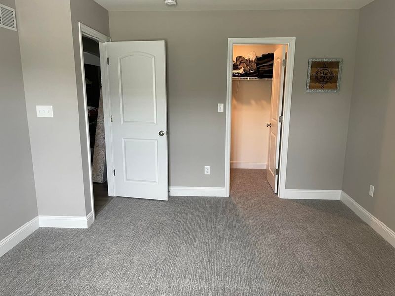 A bedroom with a carpeted floor and a walk in closet.