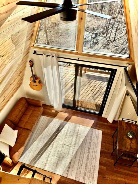 Cozy loft living room with sofa, rug, guitar, tall windows, and sliding glass door leading to a balcony