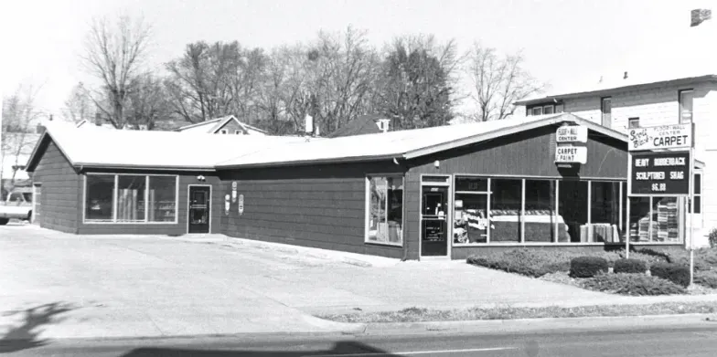 Black-and-white photo of a small roadside building with a gas station and parked car