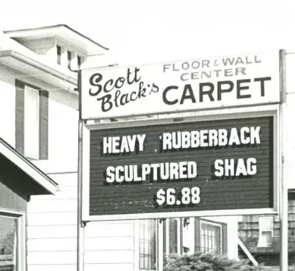 Black-and-white sign for Scott Black’s Floor & Wall Center advertising heavy rubberback sculptured shag carpet for $6.88