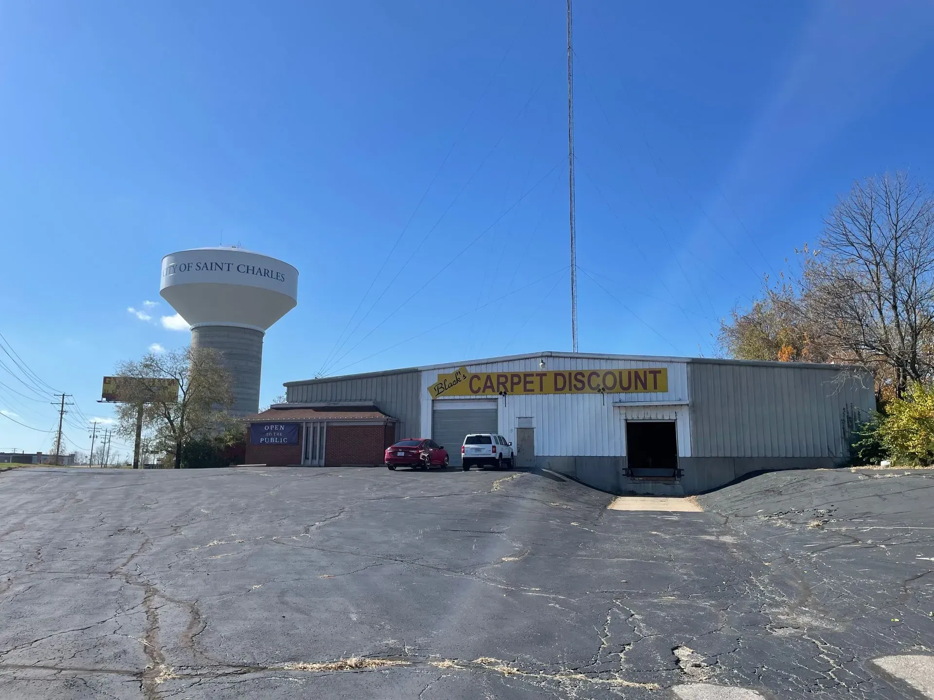 Small roadside discount store with a water tower, parked cars, and a clear blue sky.
