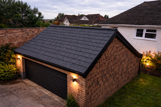 Brick garage with black roof and door; lit by warm lights; houses in background.