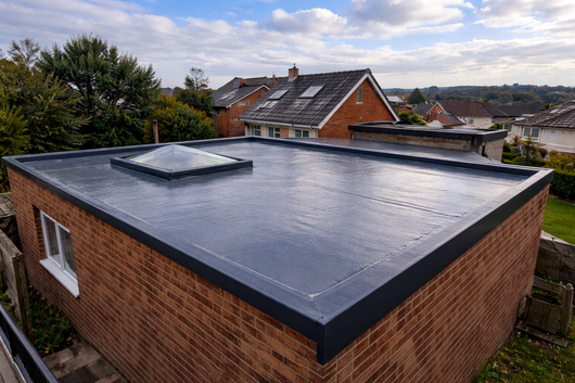 A brick building with a dark flat roof, a skylight, and a white-framed window.