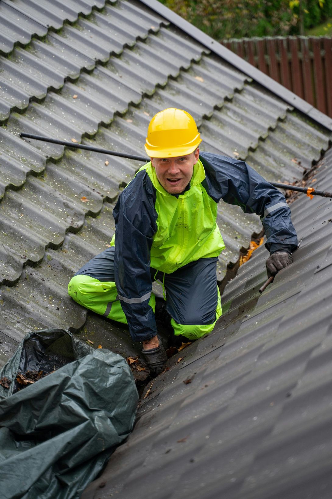 Person in rain gear and hard hat cleaning debris from a roof gutter.