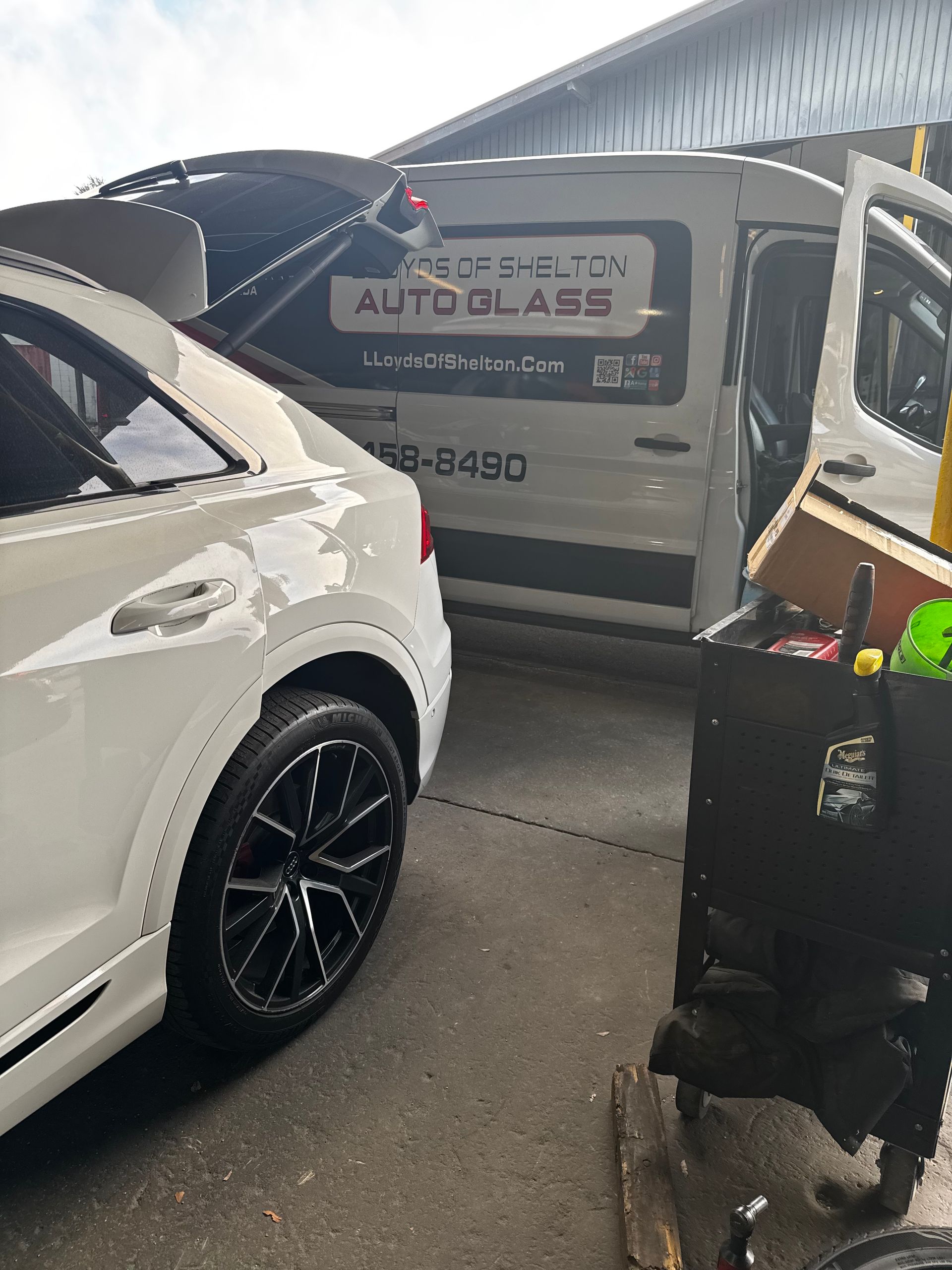 Windshield Replacement: Two cars parked under a canopy beside a rolling suitcase and bag.