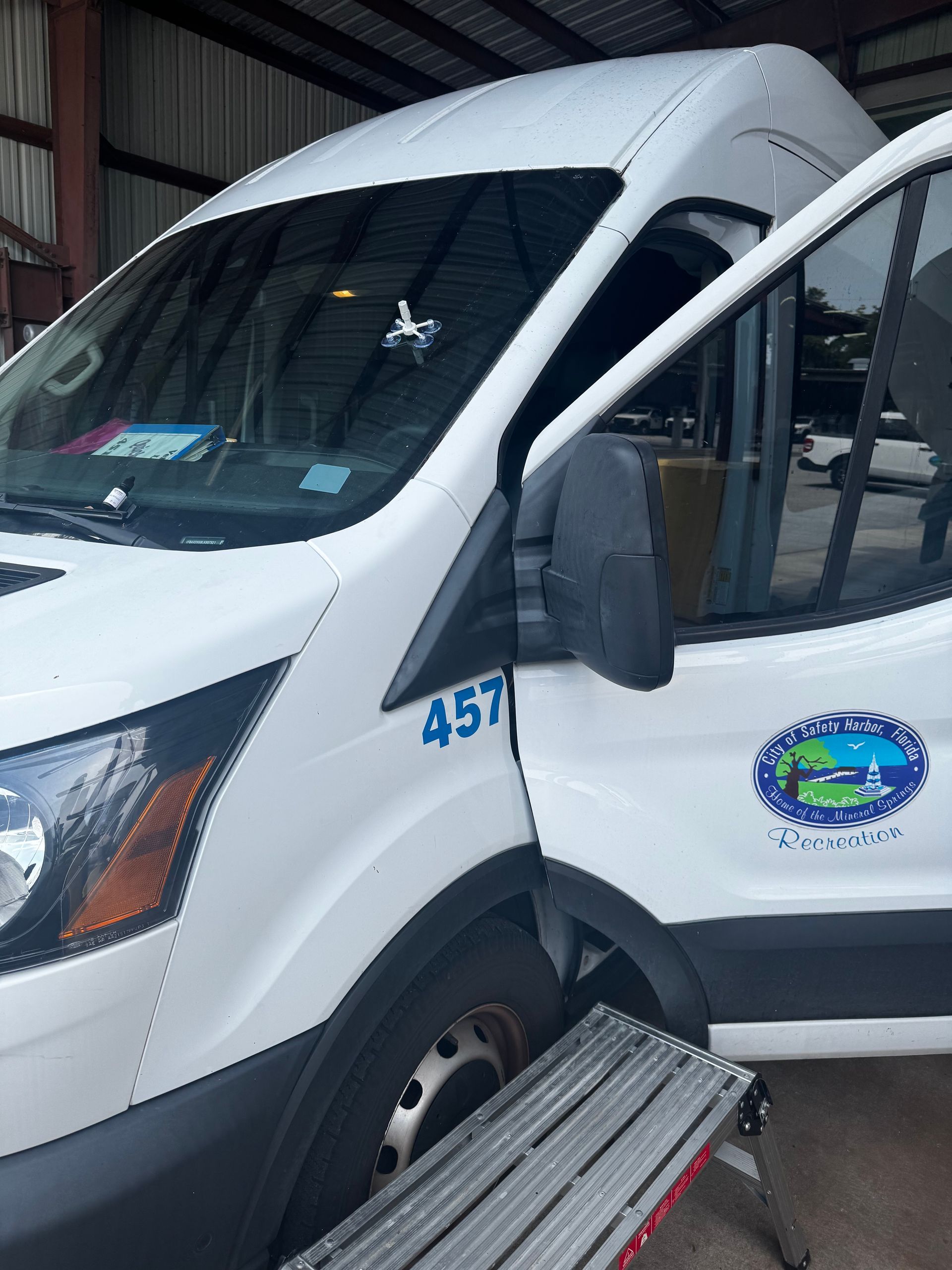 Windshield Replacement: White passenger van with open side door parked inside a garage, front wheel visible, blue logo on the door