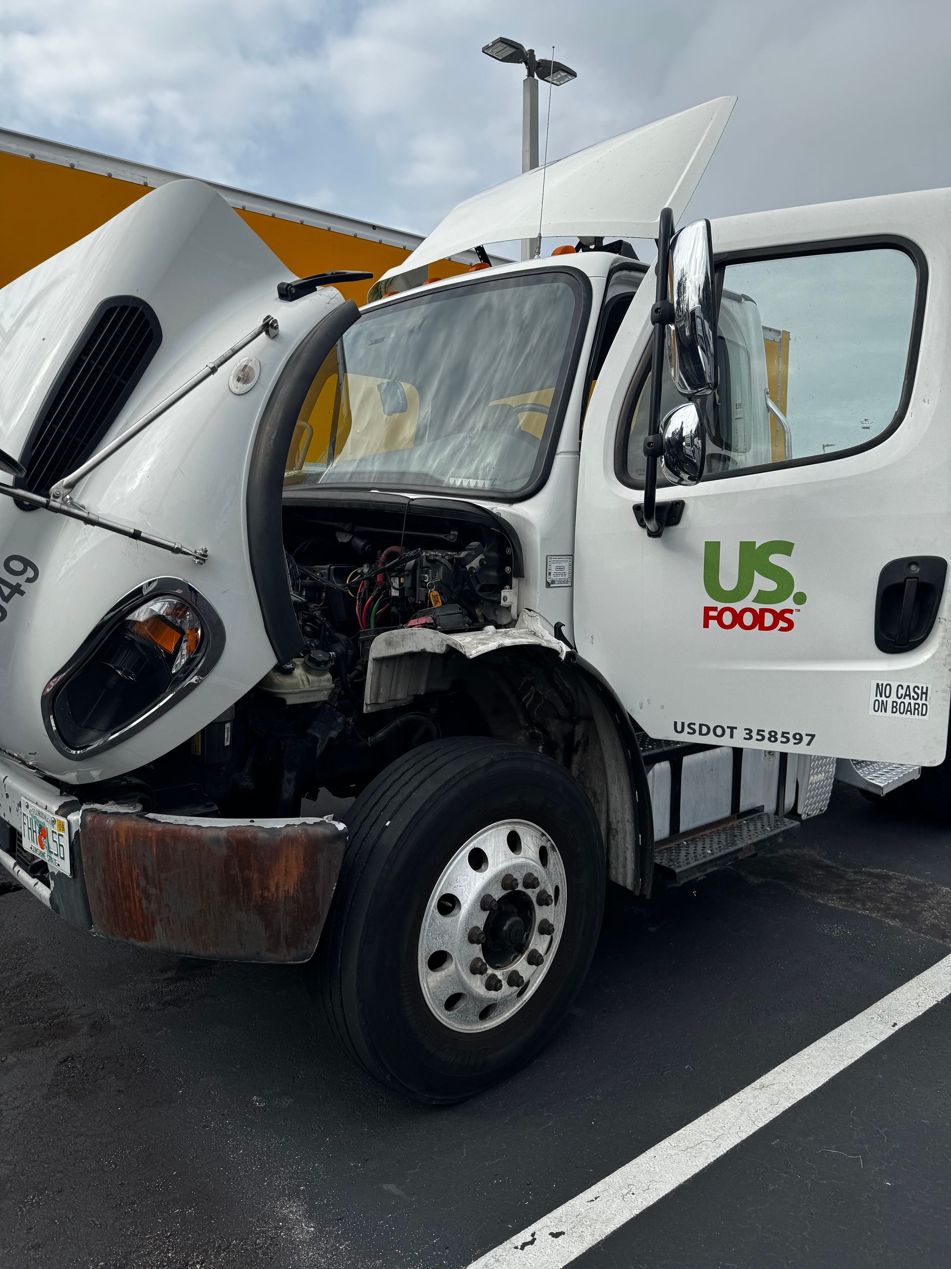 Windshield Replacement: Damaged white US Foods box truck with crumpled cab on a highway shoulder