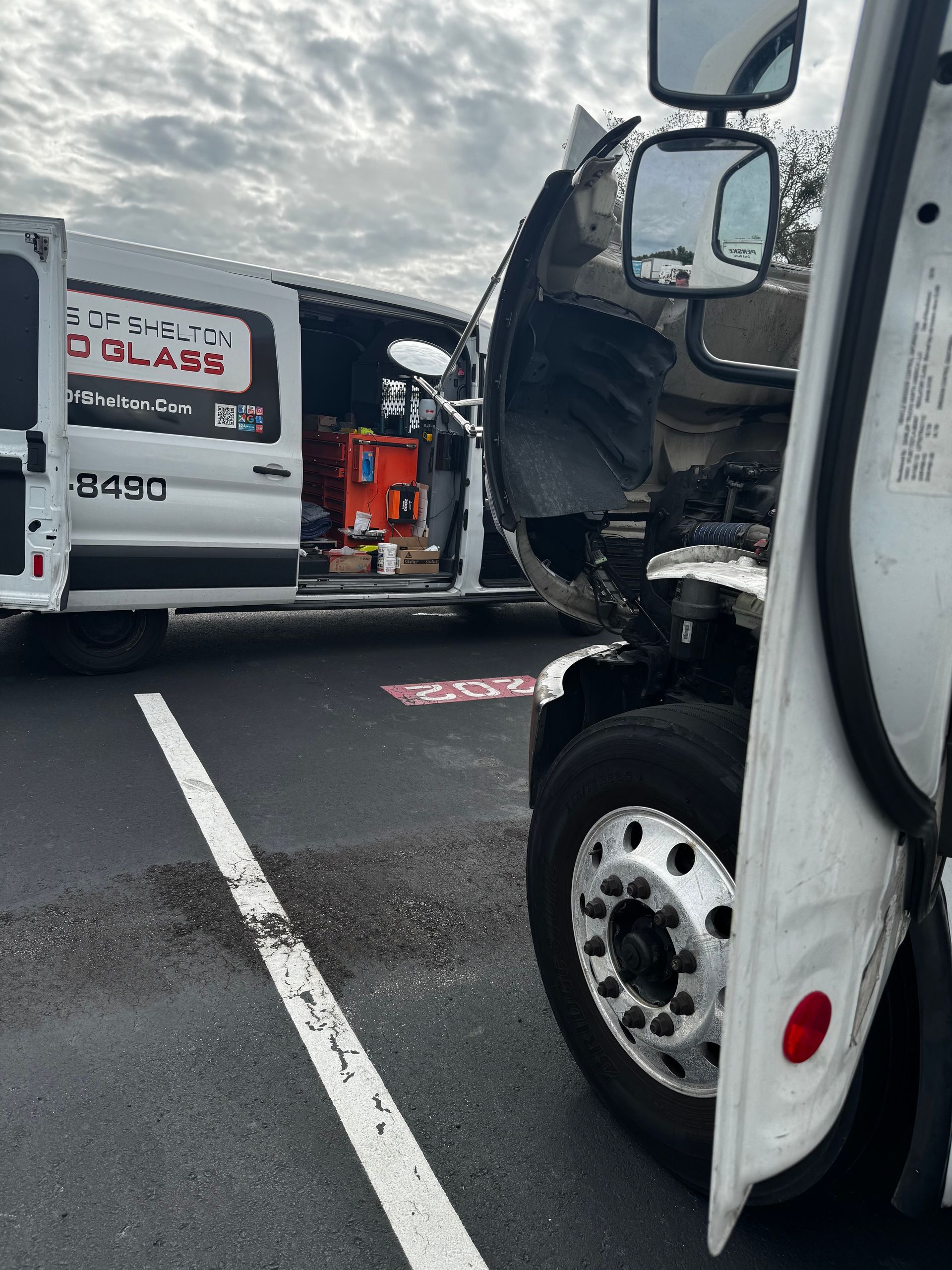 Commercial Fleet Glass Replacement: Collision scene with two damaged white trucks on a wet road, debris visible between them.