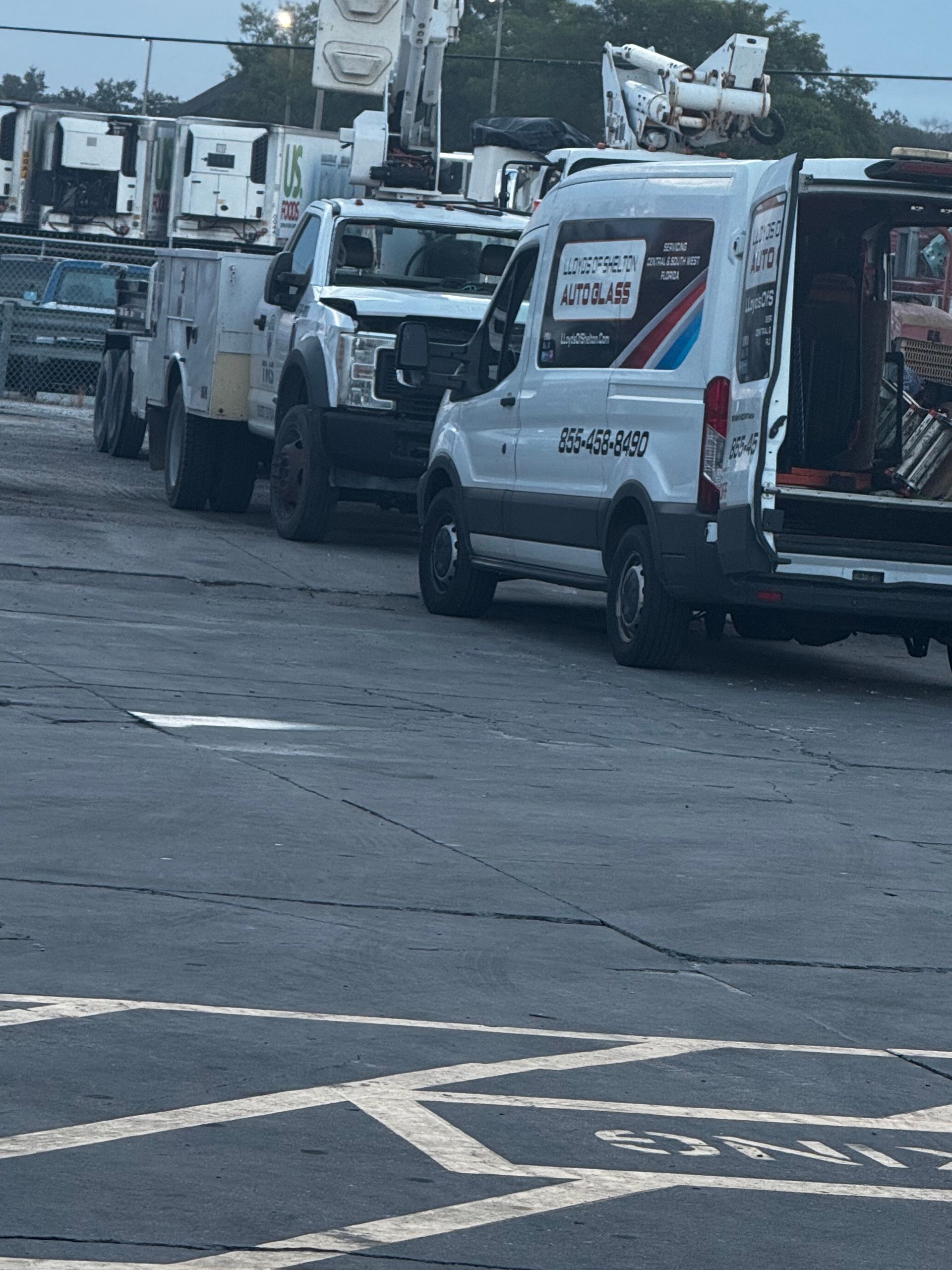 Commercial Fleet Glass Replacement: White utility trucks lined up on a wet street, with utility buckets and equipment in the background.