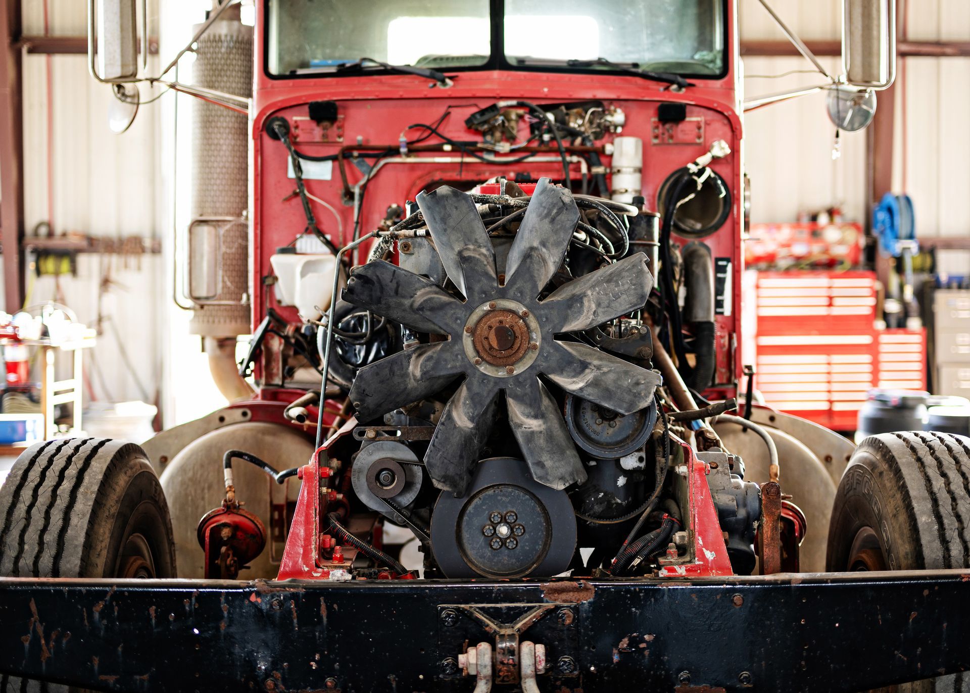 Exposed car engine block mounted on a stand, with a white vehicle in the background.