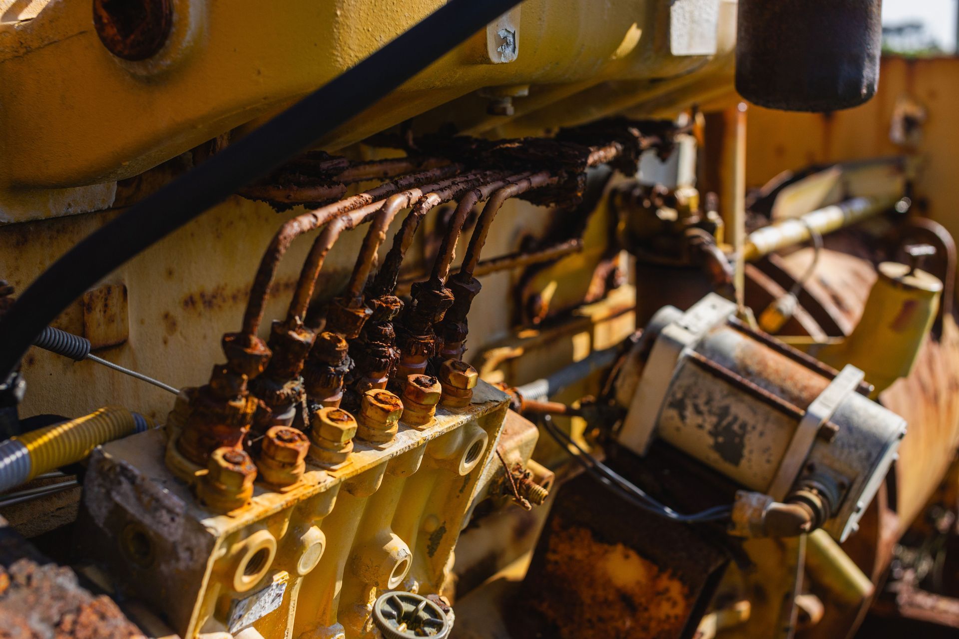 Close-up of rusty yellow hydraulic machinery with pipes, valves, and metal fittings in a worksite setting