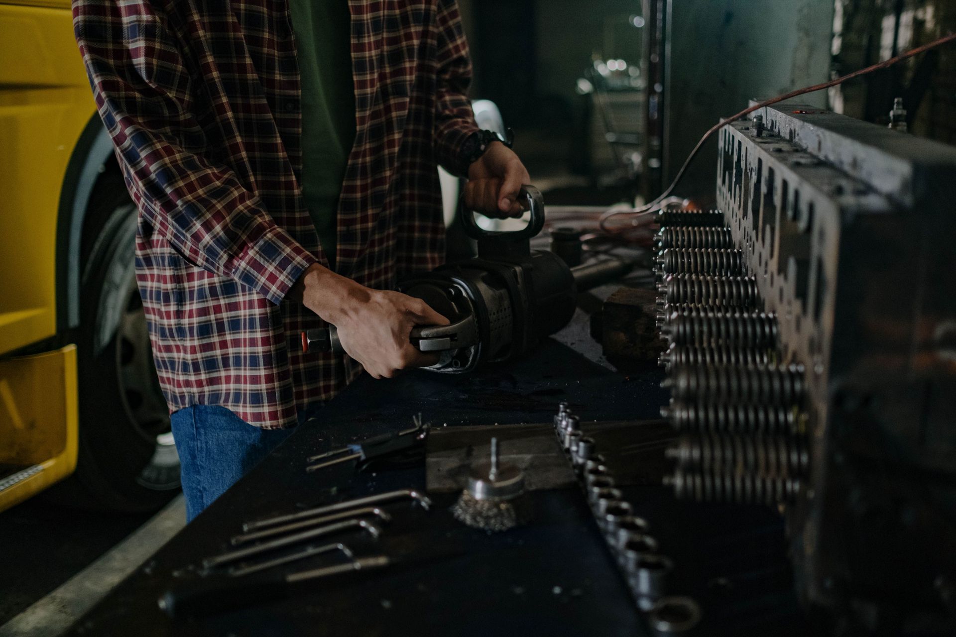Mechanic using a power tool to work on metal parts at a workshop bench
