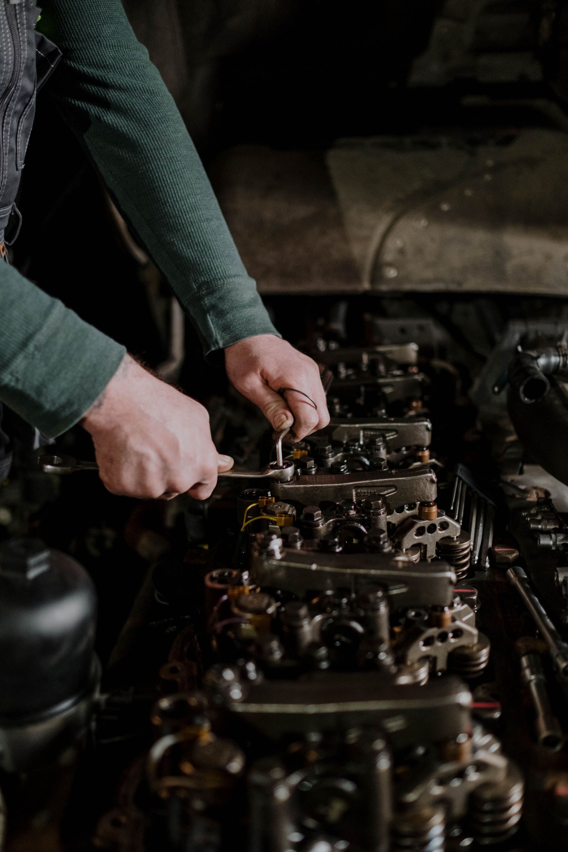 Hands working on an engine, tightening bolts inside a dimly lit workshop