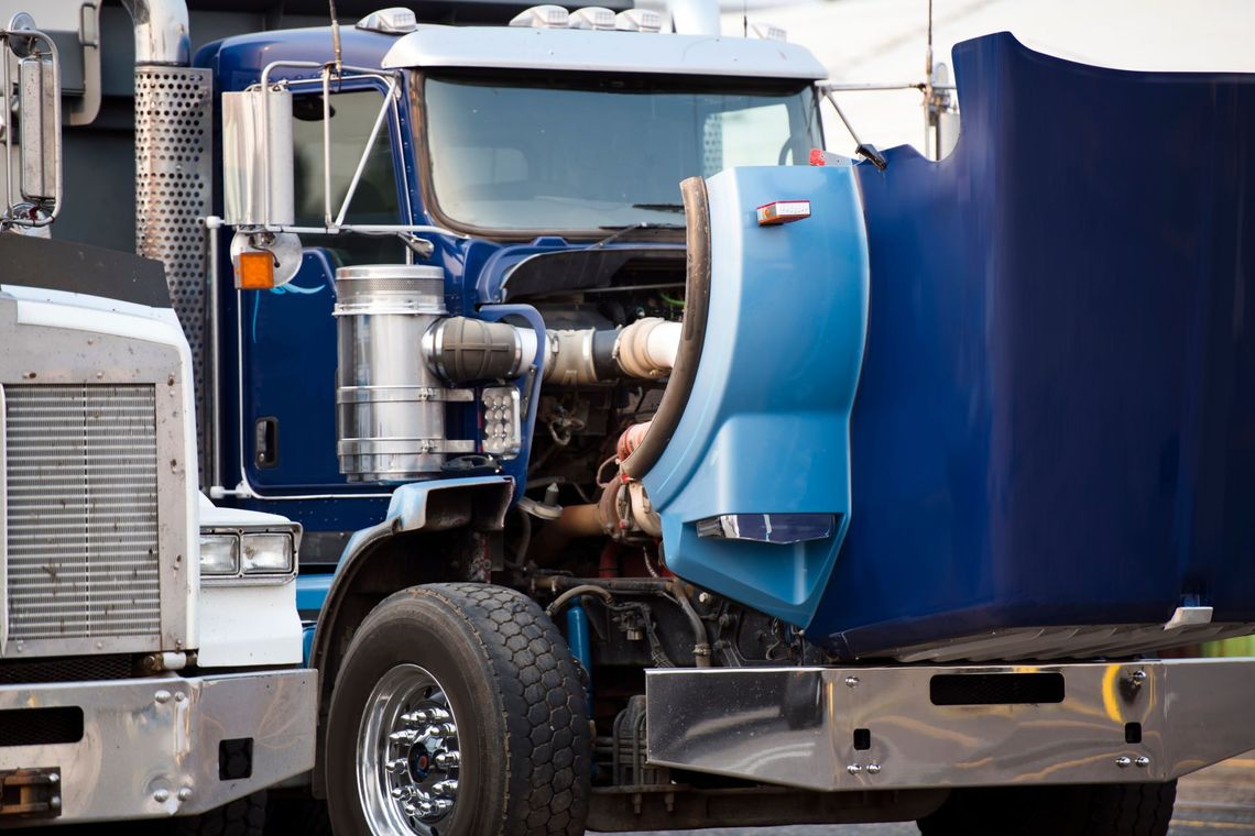 Blue semi-truck cab parked beside a white truck, close-up of front and engine area