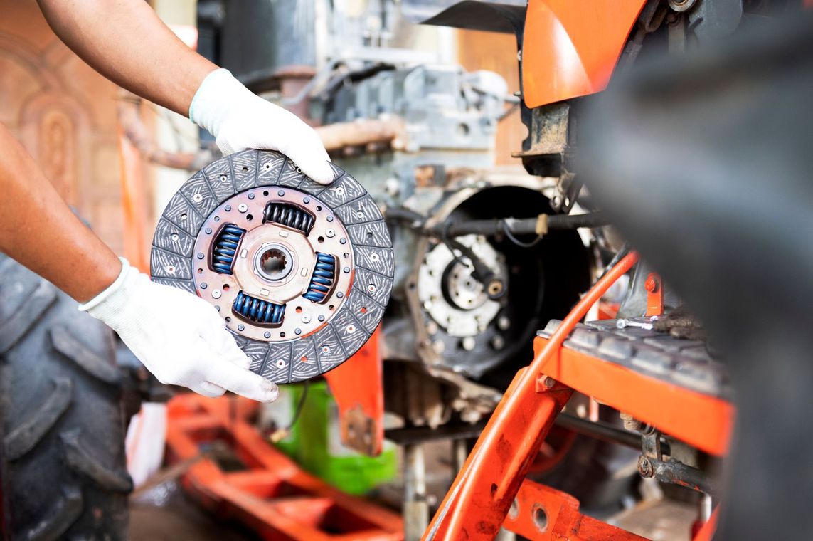 Mechanic holding a clutch disc in a car repair shop, with orange lift equipment in the background